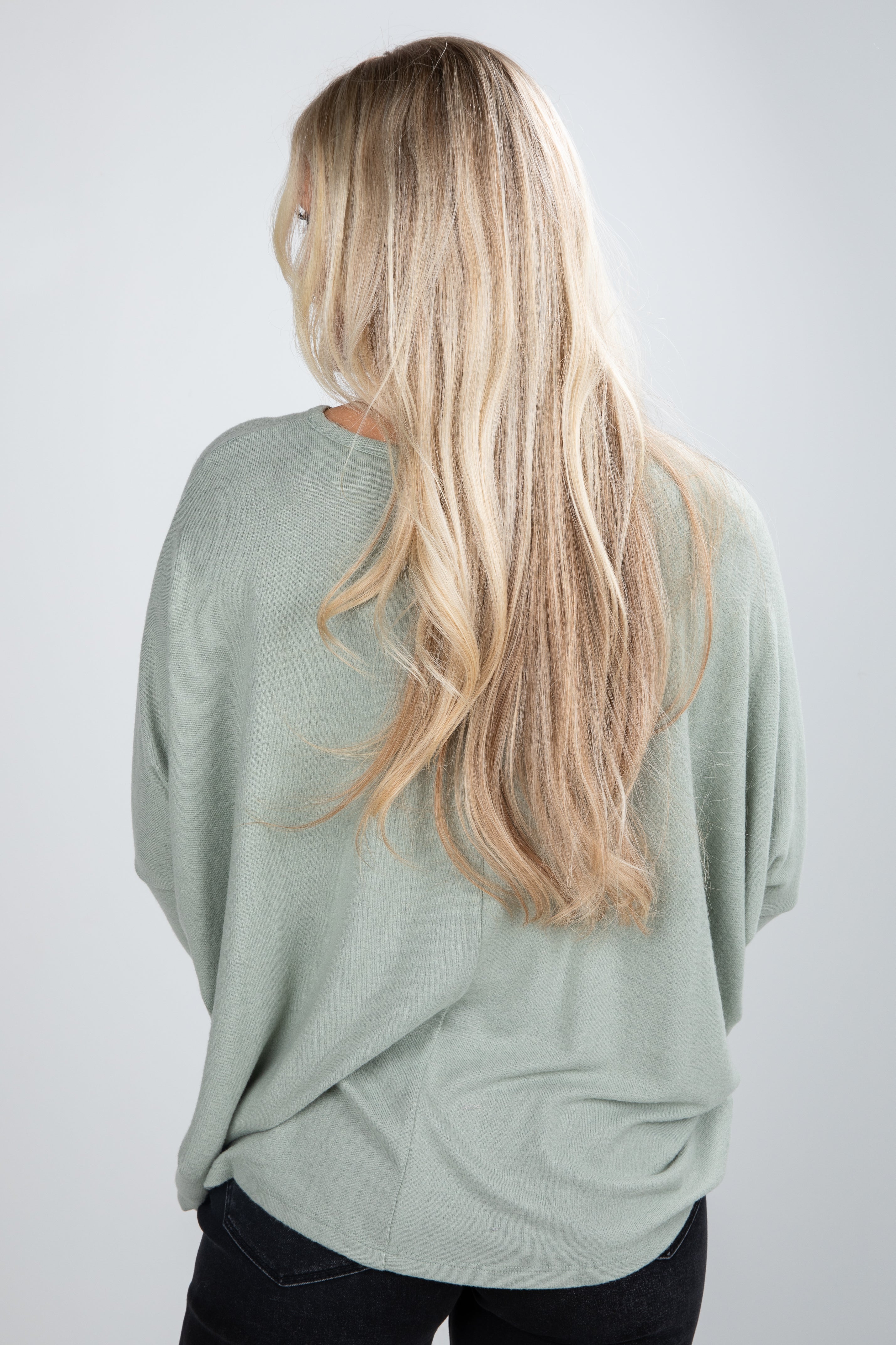 Person wearing a light green sweater with long blonde hair on a plain background