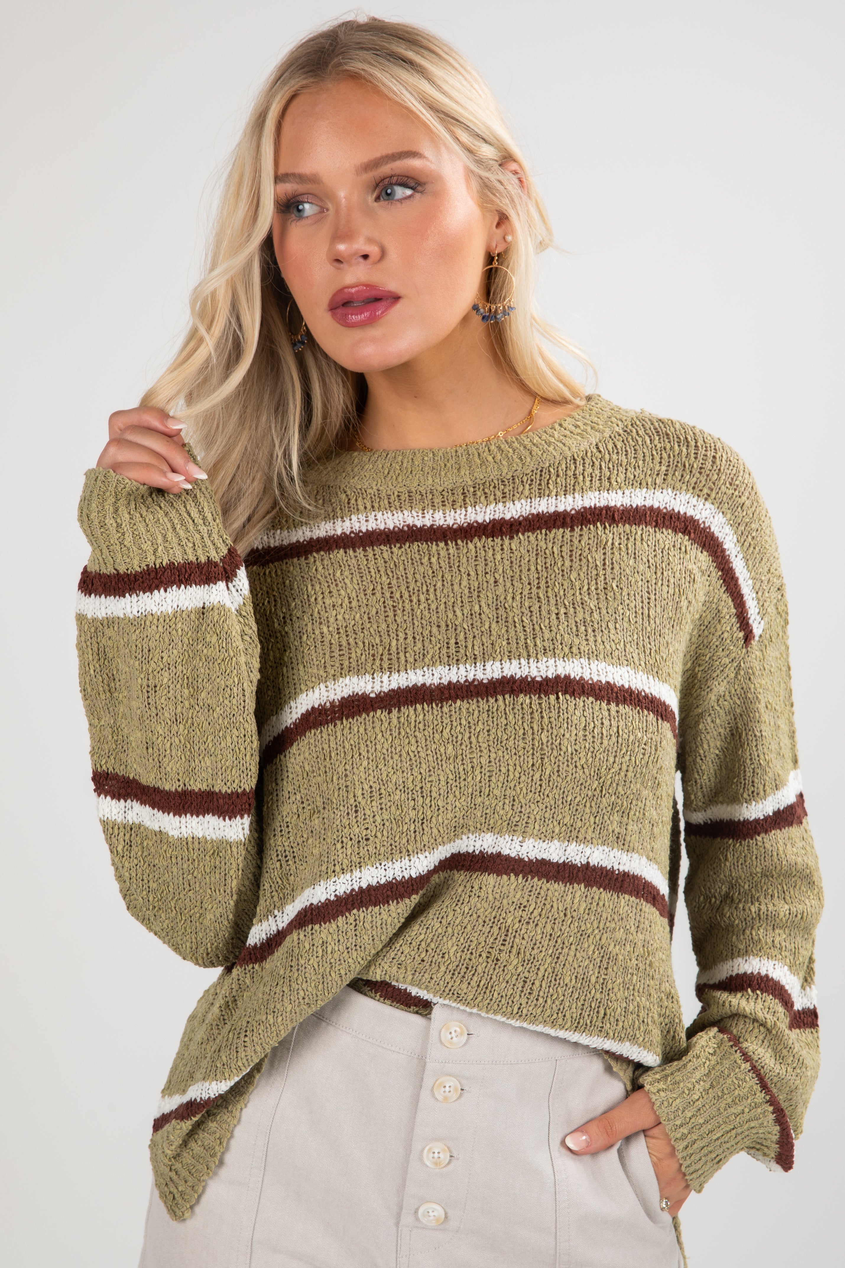 Woman wearing a green sweater with brown and white stripes on a plain background
