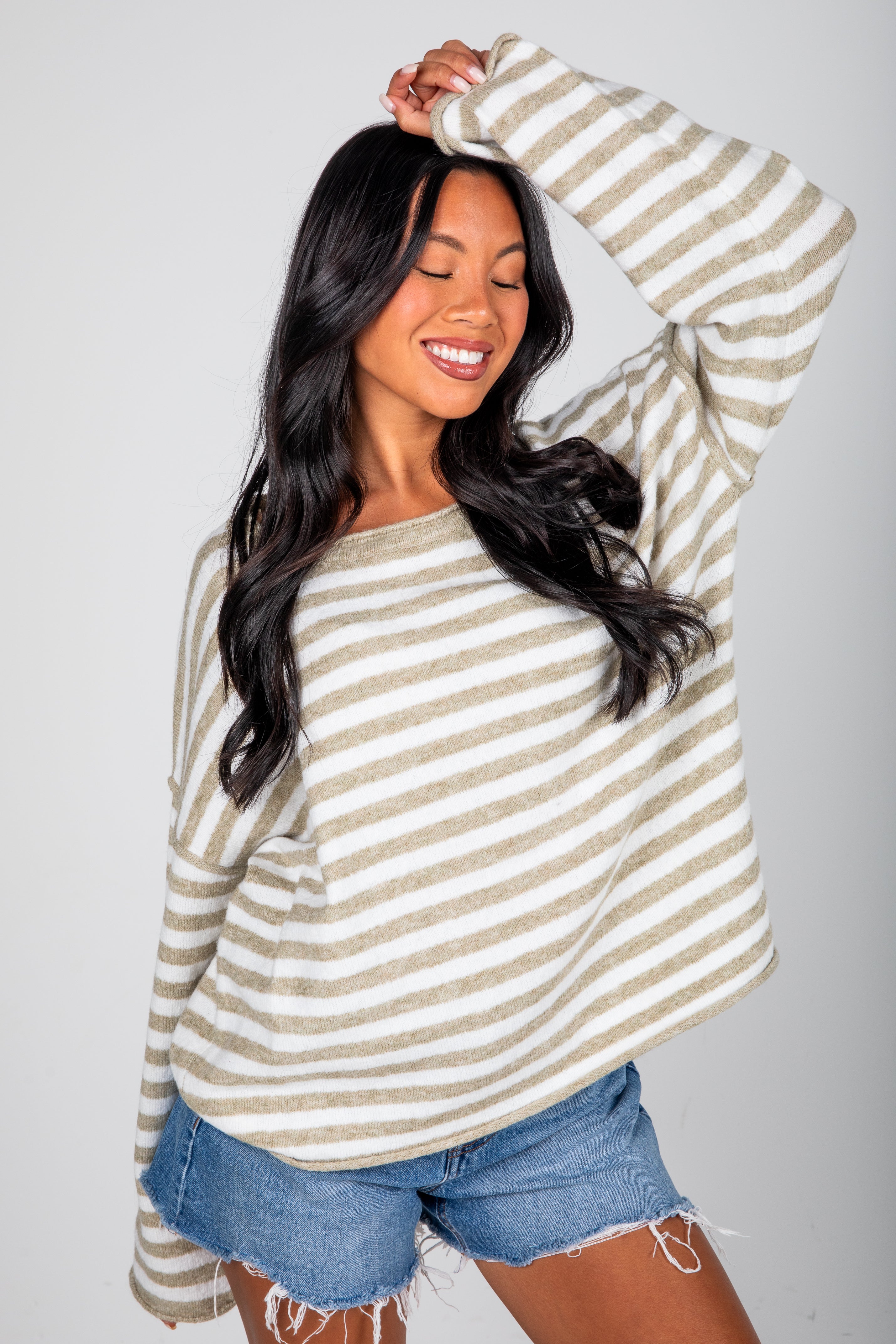 Woman wearing a striped long-sleeve top and denim shorts against a plain background
