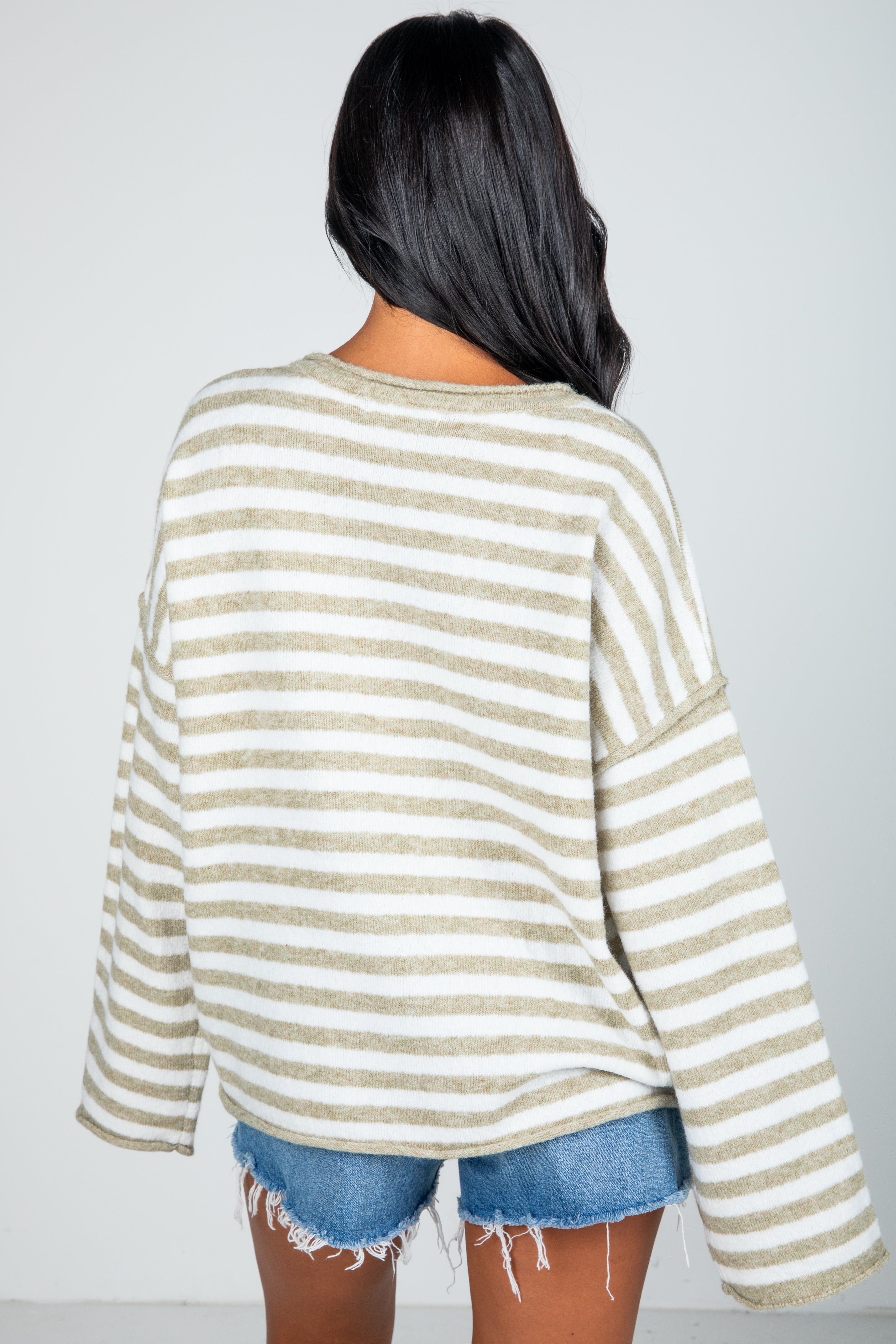 Person wearing a striped sweater and denim shorts on a plain background