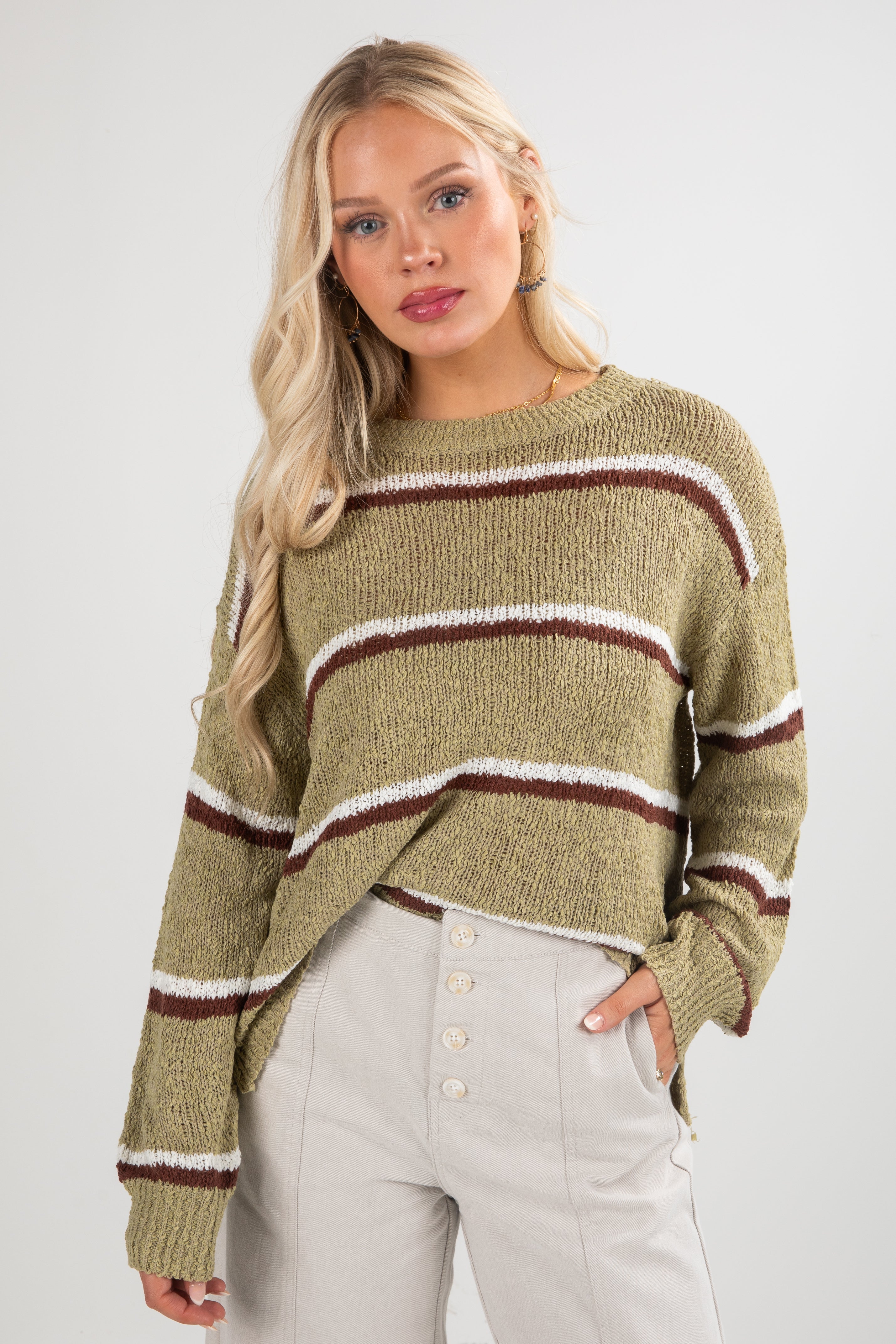 Woman wearing a green sweater with brown and white stripes on a plain background