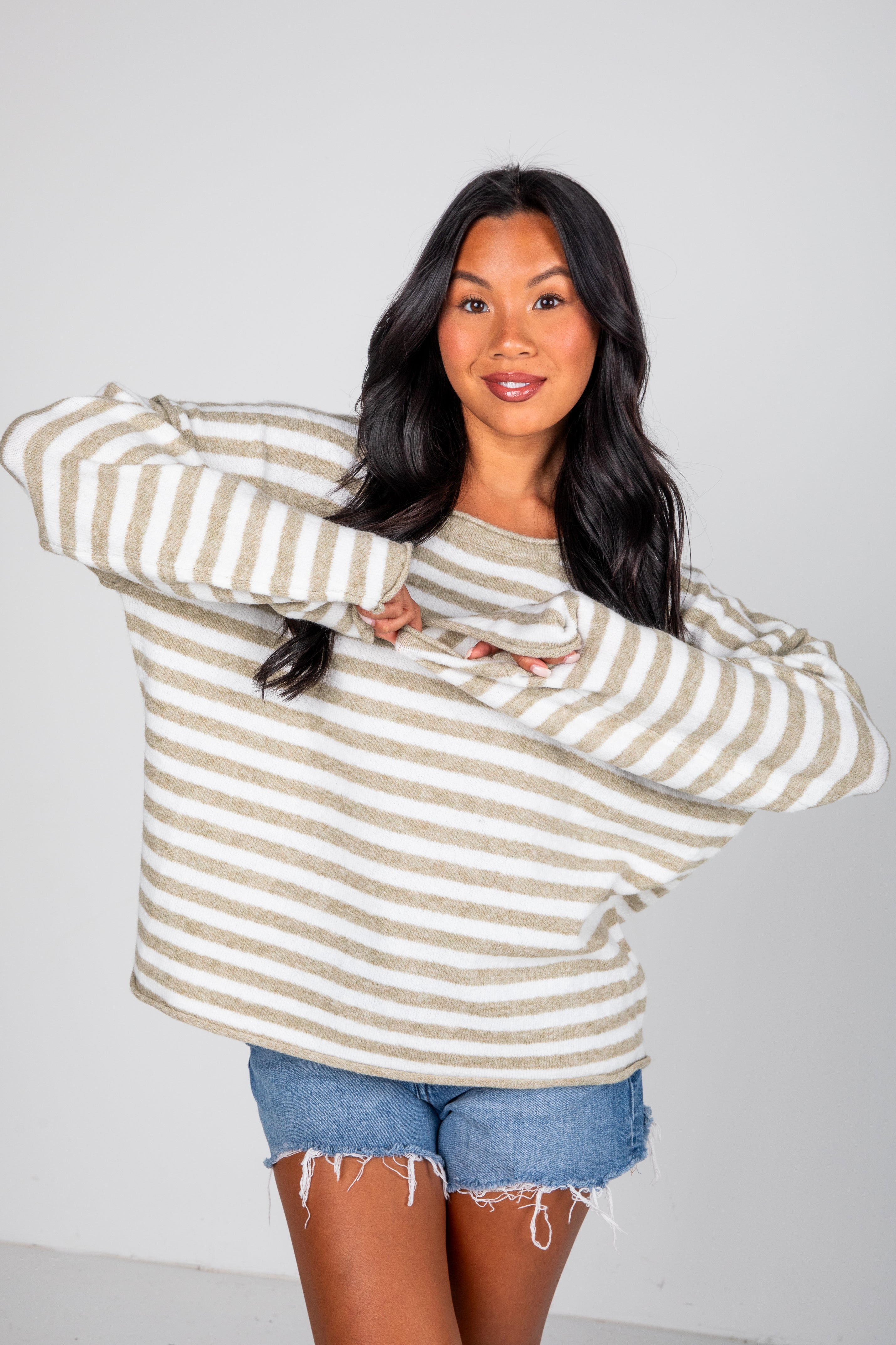 Woman wearing a striped sweater and denim shorts on a plain background