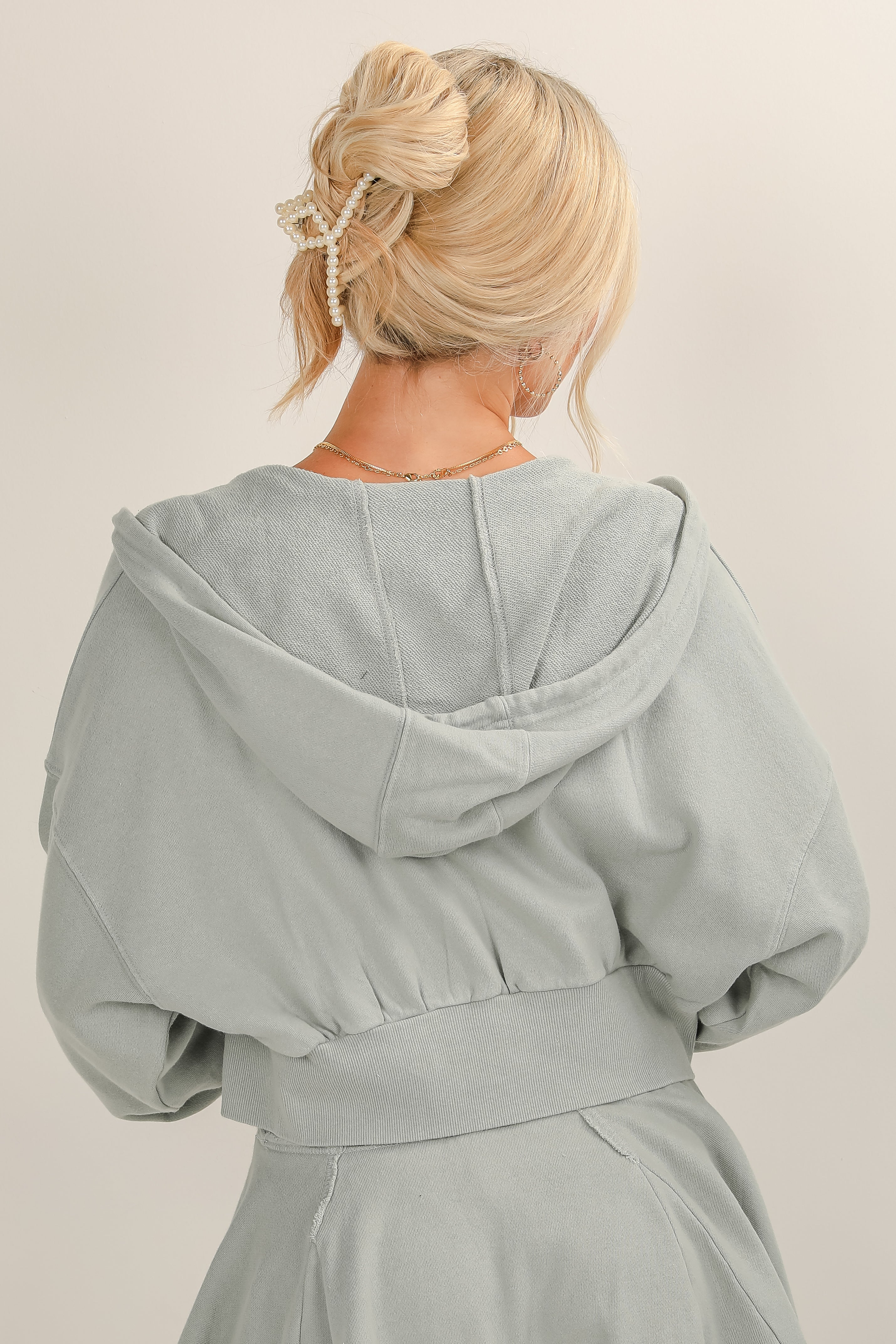 Person wearing a light gray hooded garment against a plain background