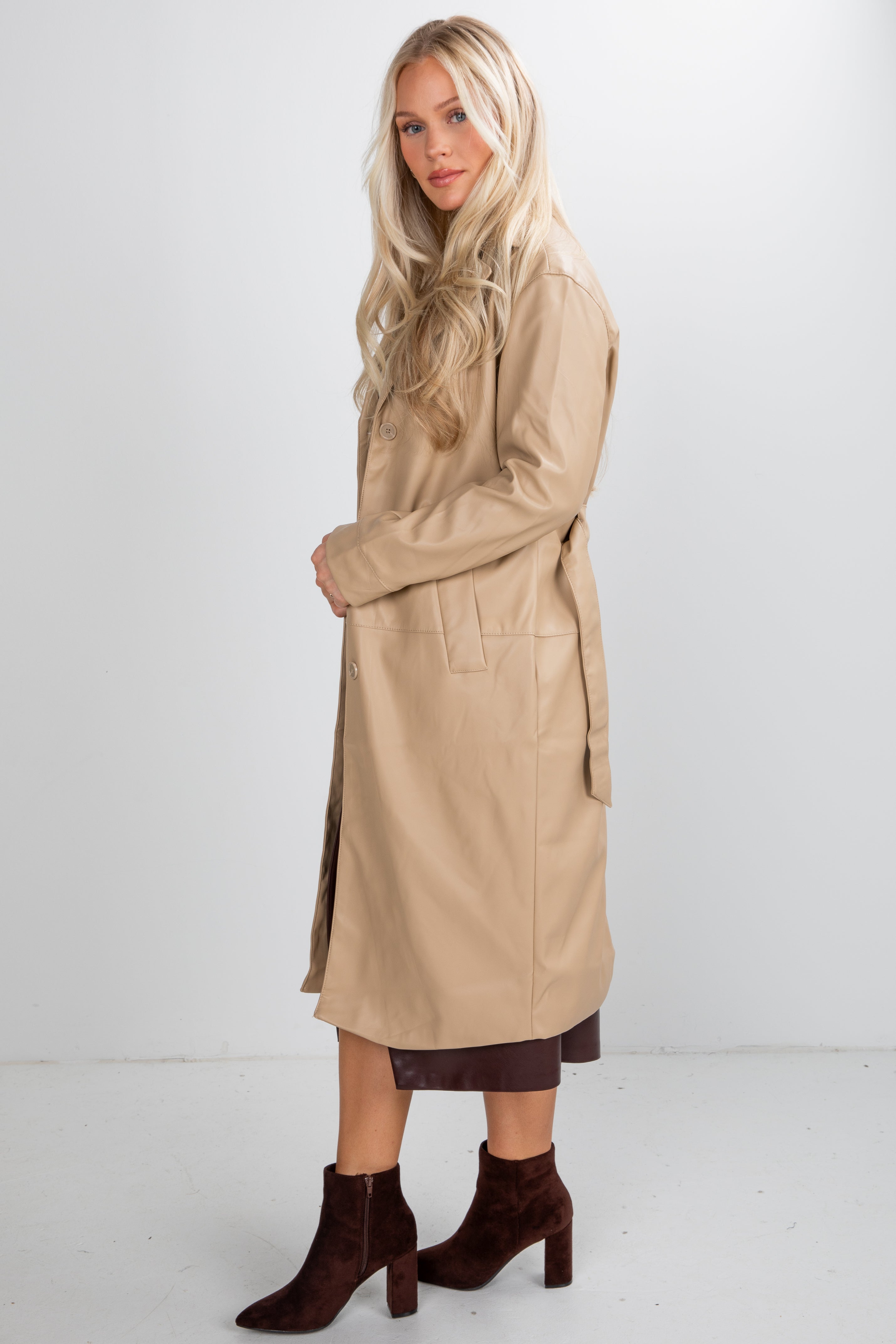 Woman wearing a beige trench coat and brown boots on a white background