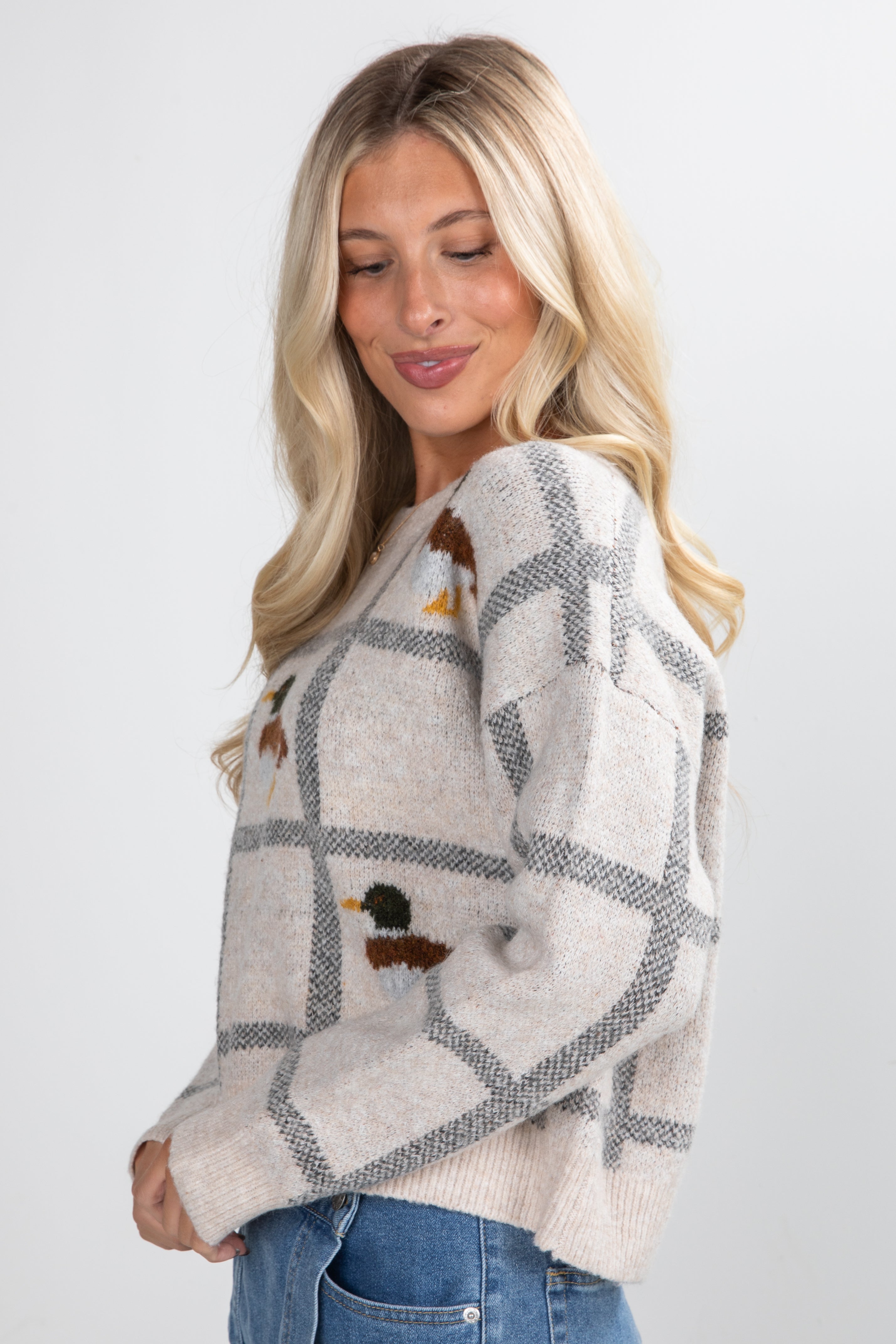 Woman wearing a patterned sweater with duck designs on a plain background
