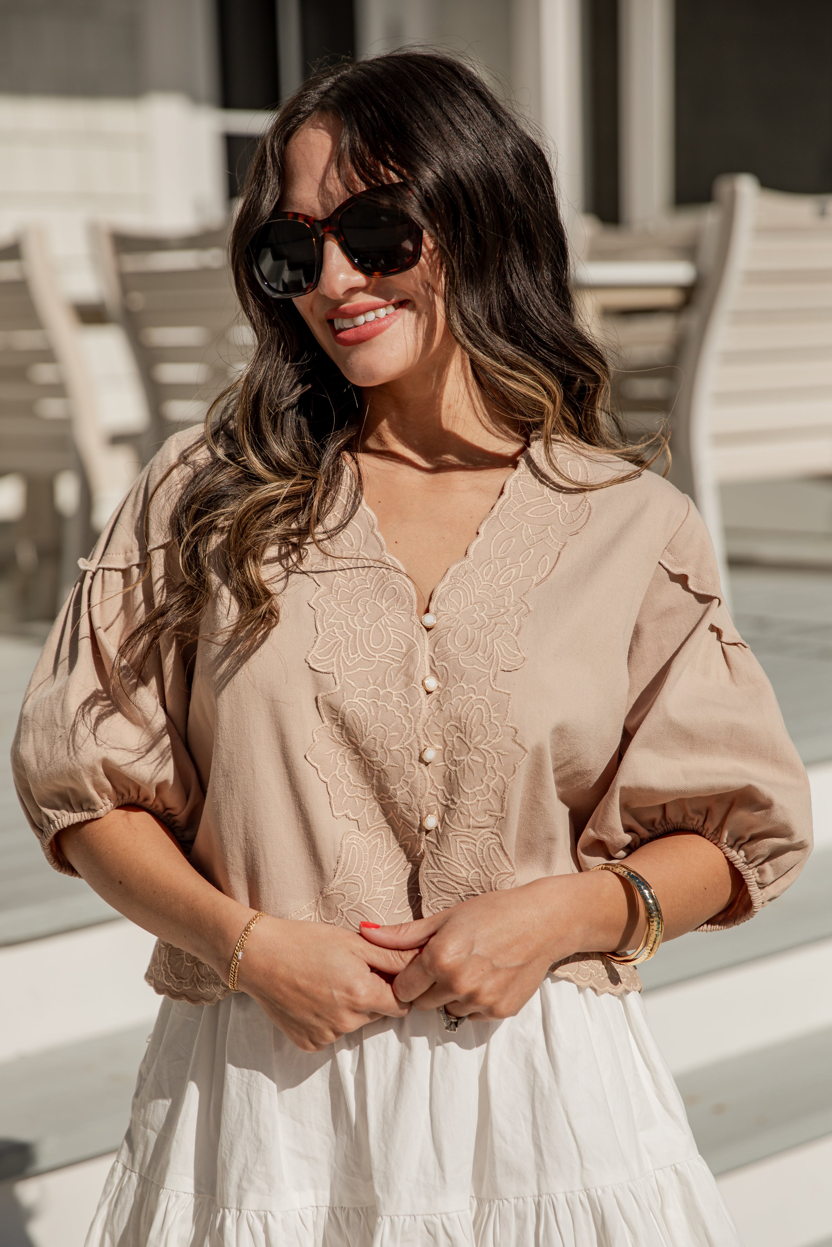 Woman wearing a beige blouse and sunglasses outdoors