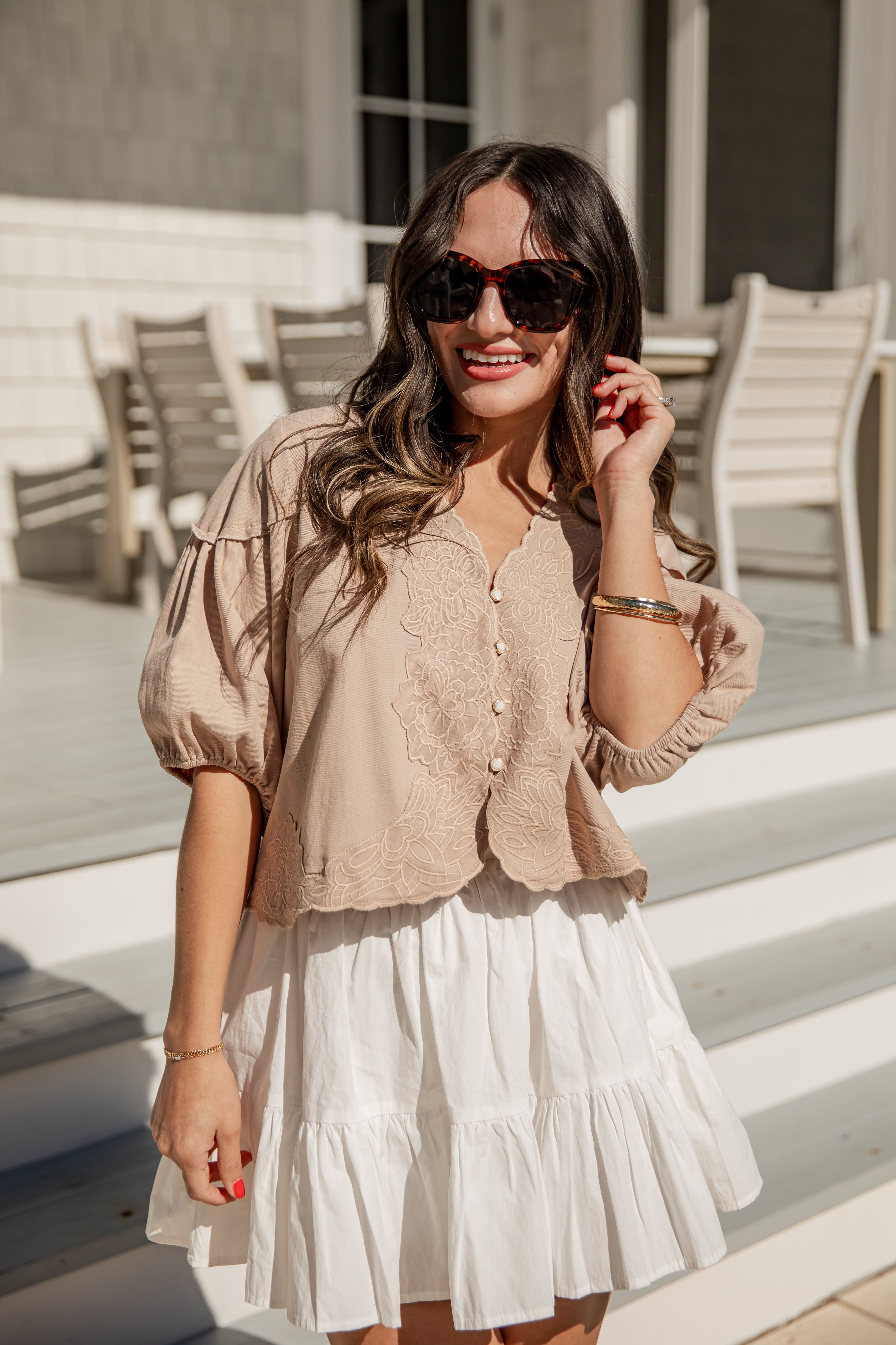 Woman wearing a beige blouse and white skirt outdoors.