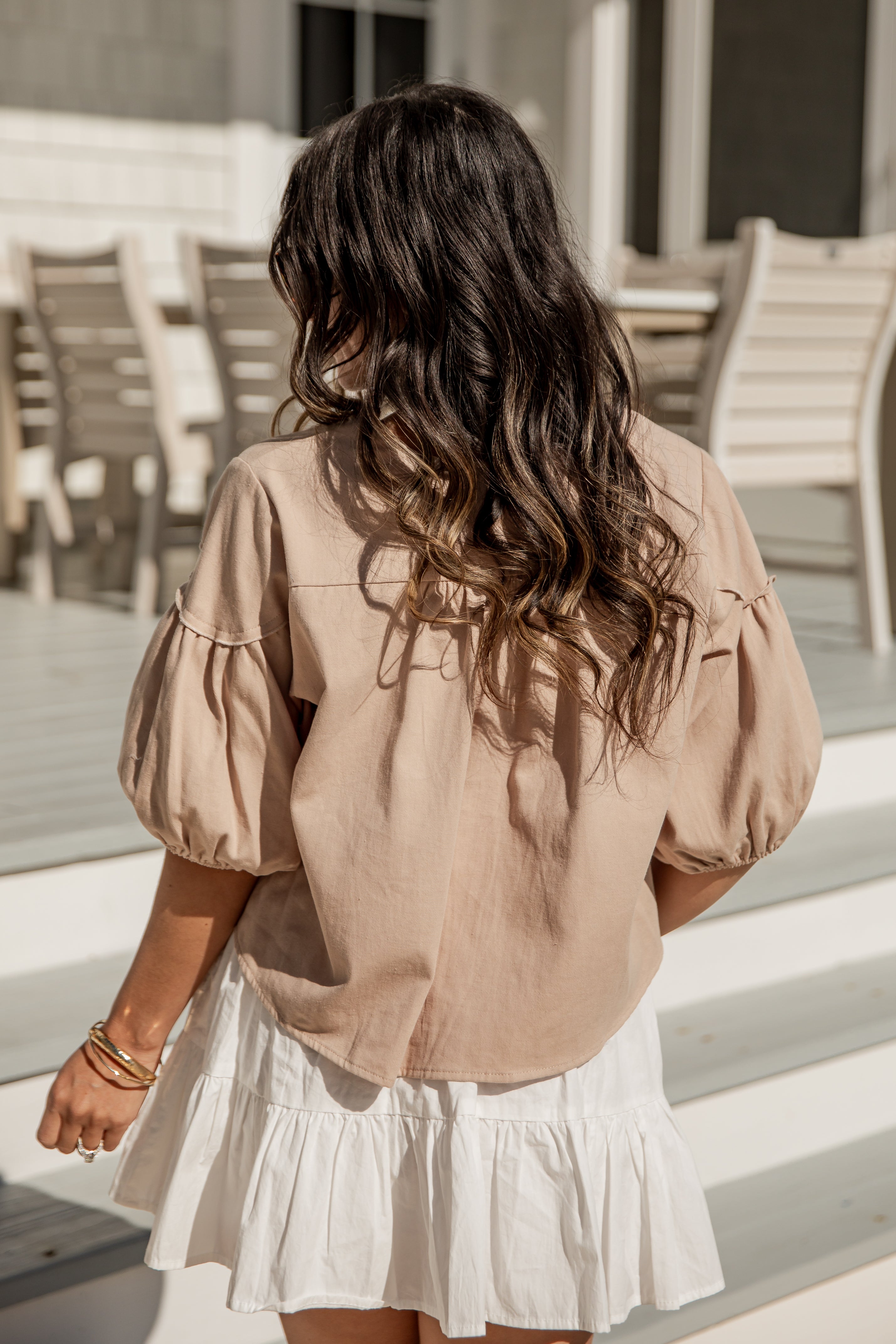 Woman wearing a beige blouse and white skirt standing on steps with chairs in the background