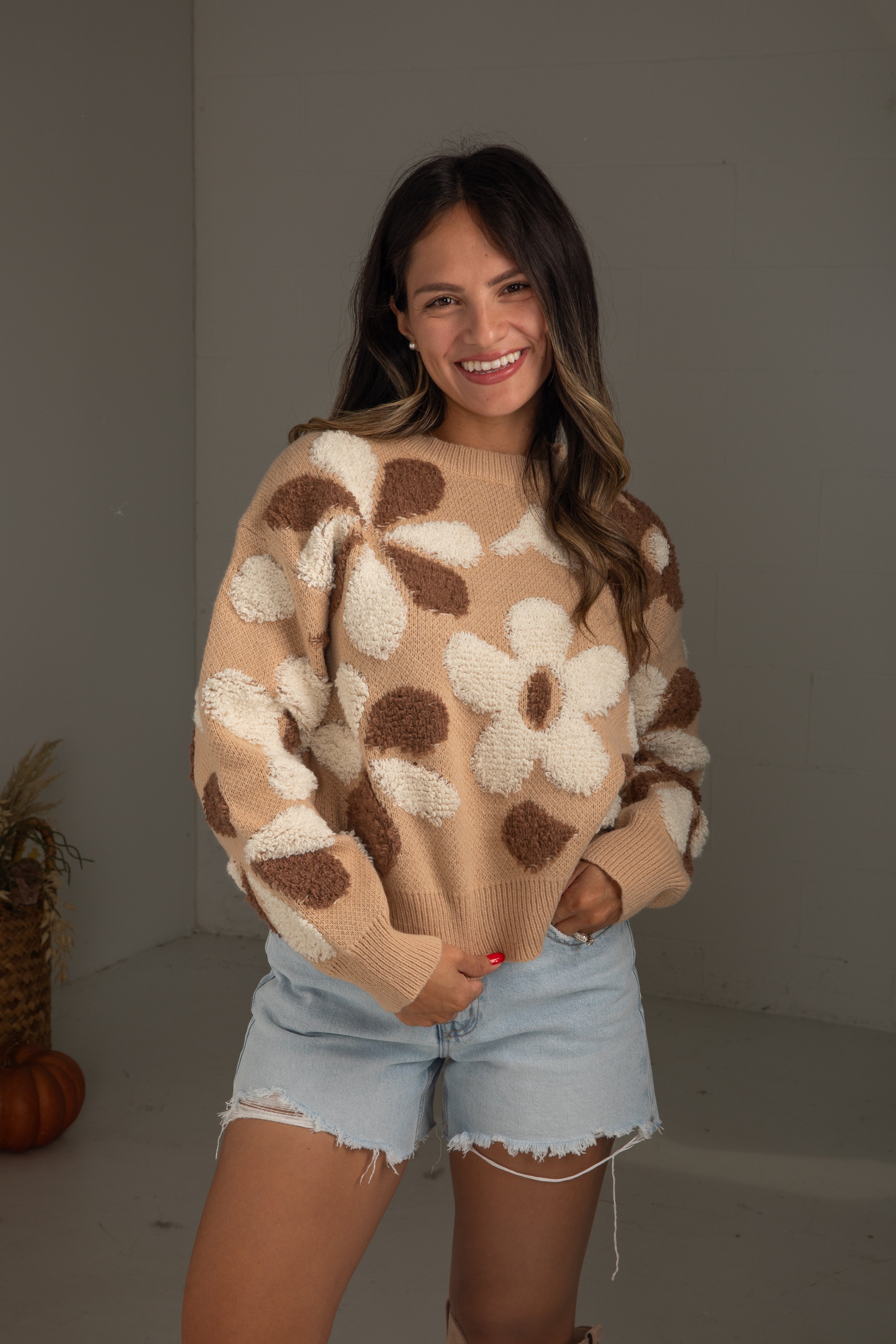 Woman wearing a beige sweater with floral patterns and denim shorts indoors.