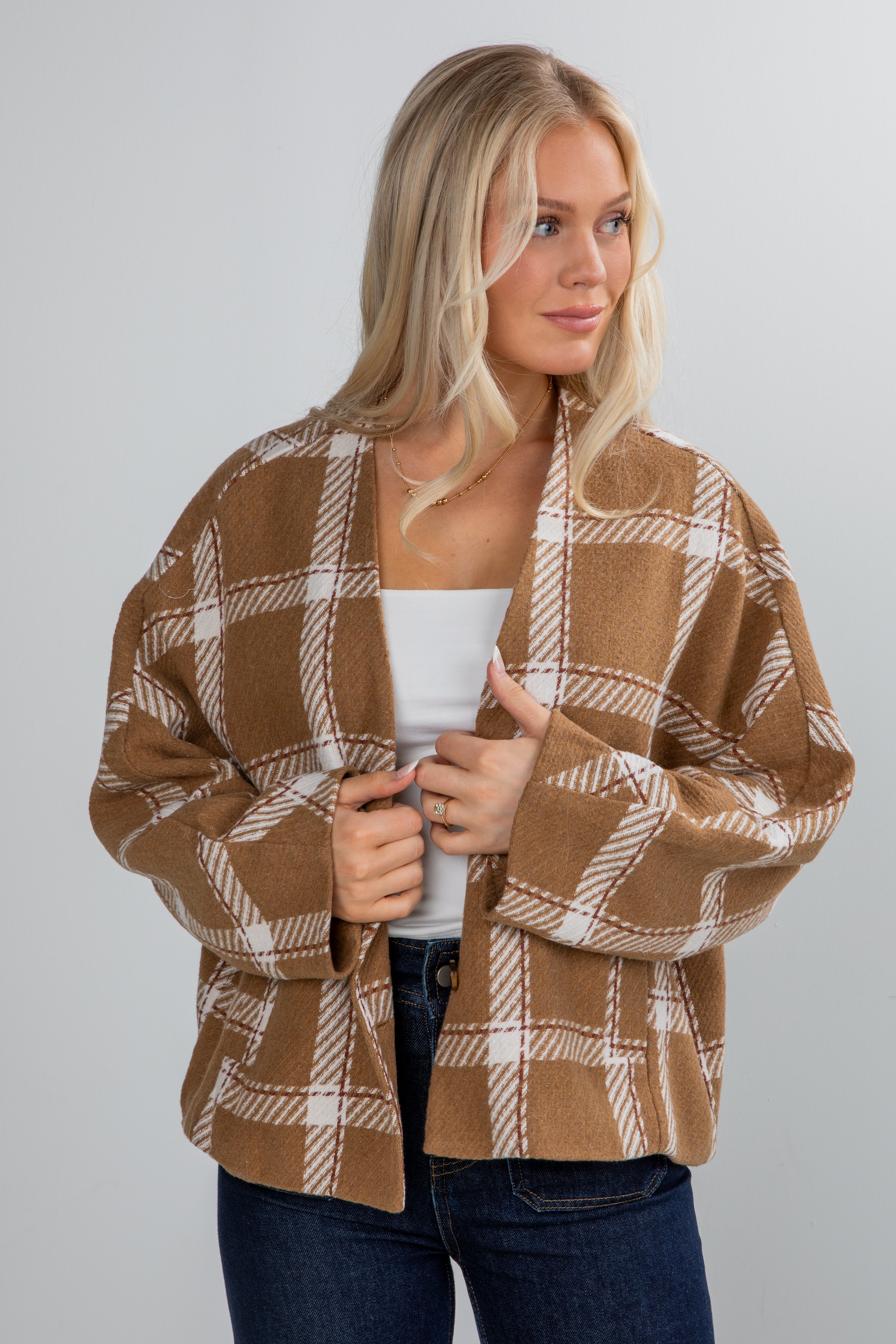 Woman wearing a brown and beige plaid cardigan on a plain background
