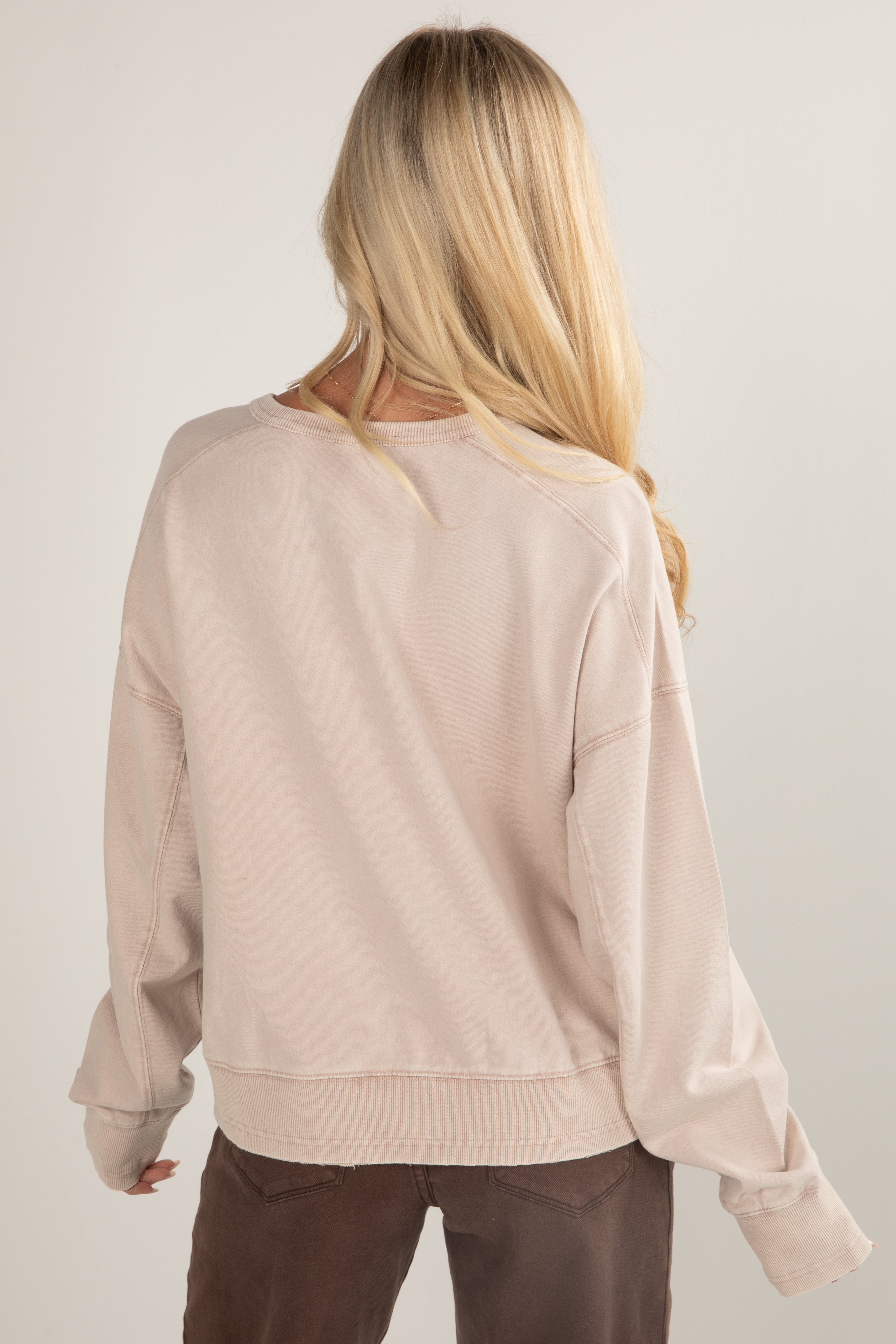 Woman wearing a beige sweater and brown pants against a plain background