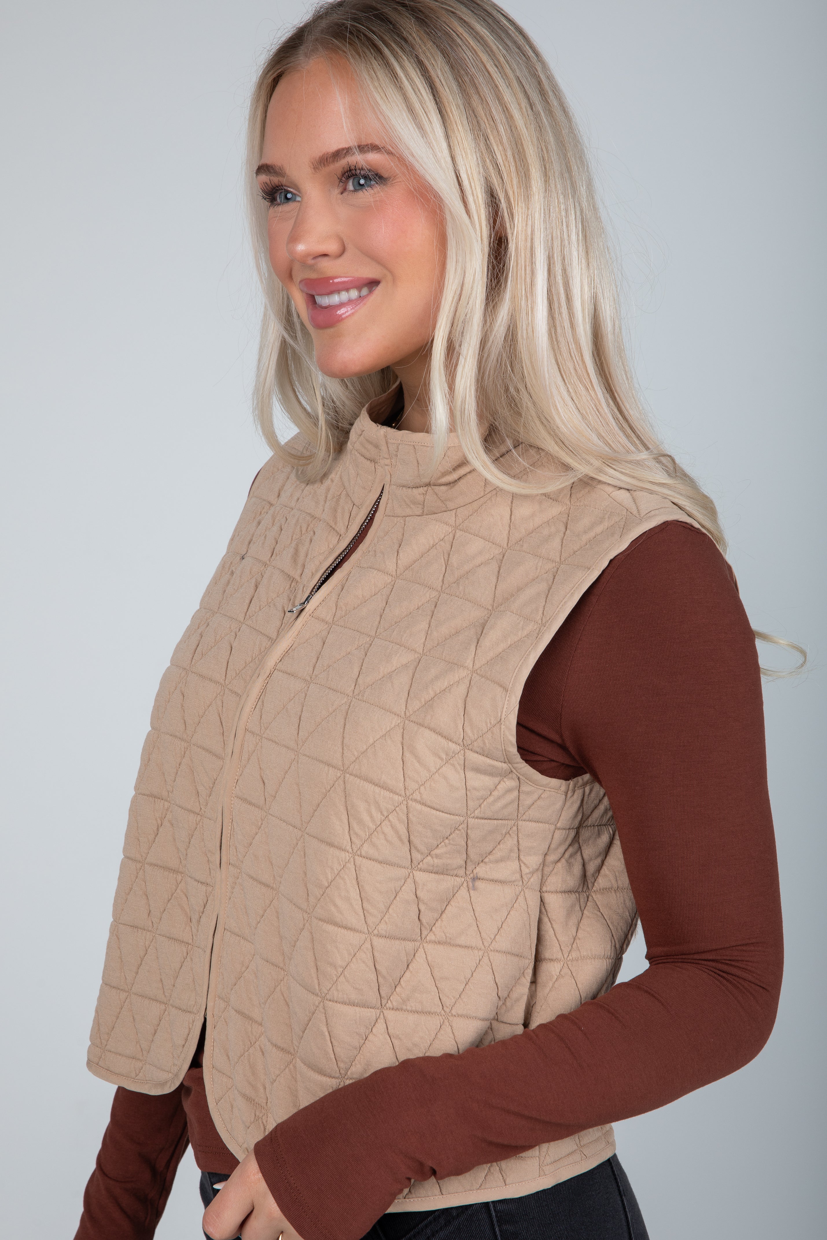 Woman wearing a beige quilted vest over a brown long-sleeve shirt against a plain background