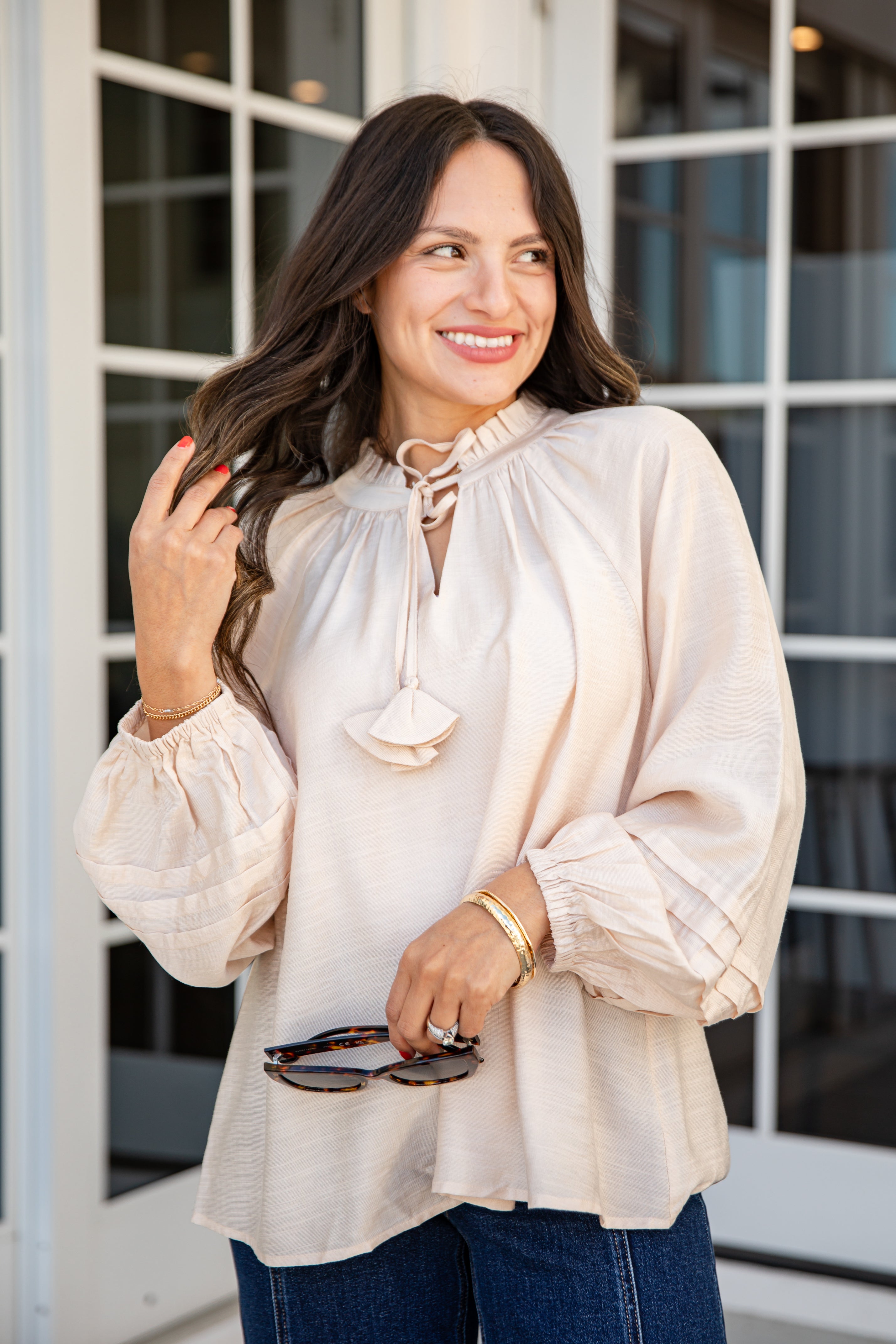 Woman wearing a beige blouse with a tie detail in an outdoor setting