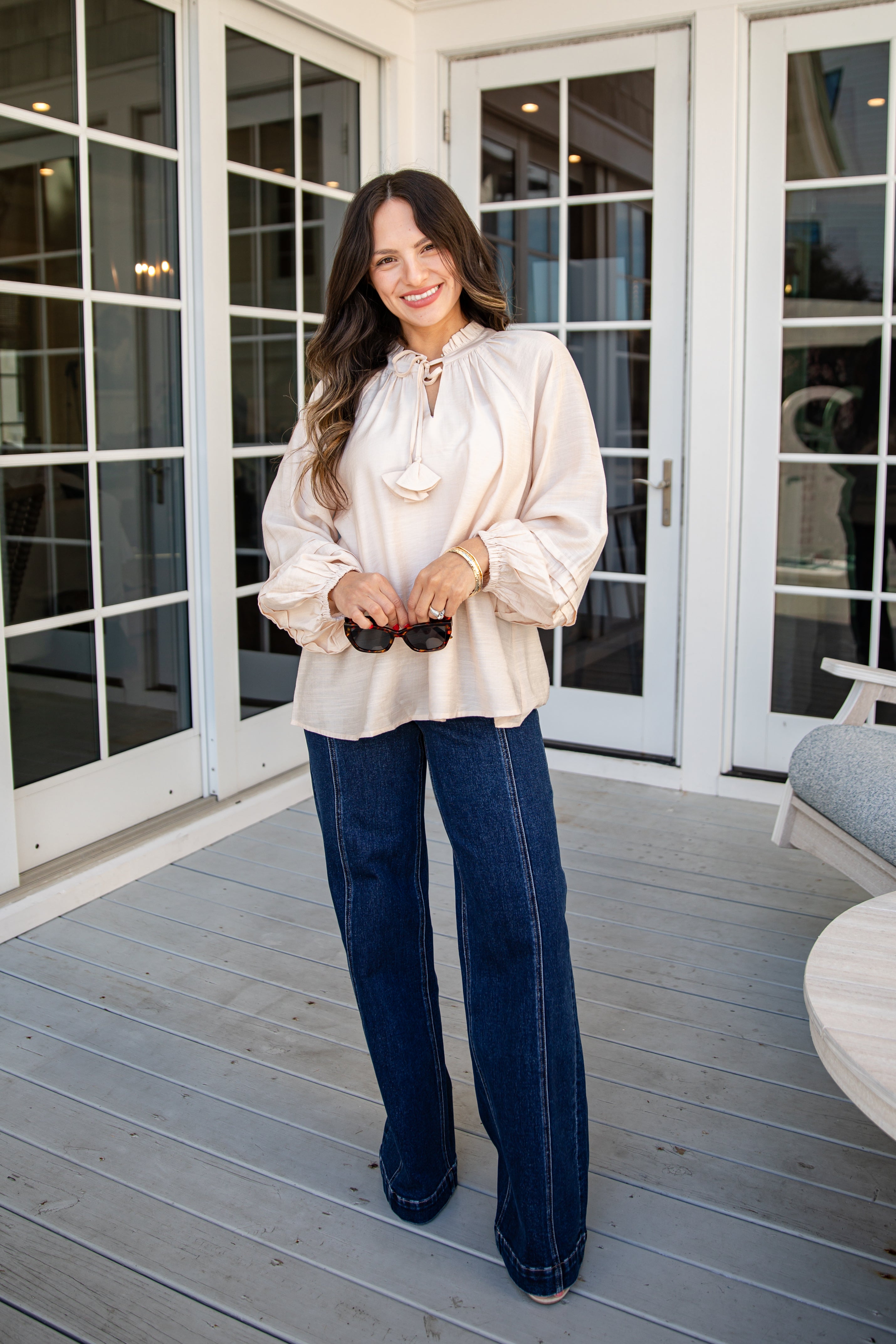 Woman in a white blouse and blue jeans standing on a wooden deck.