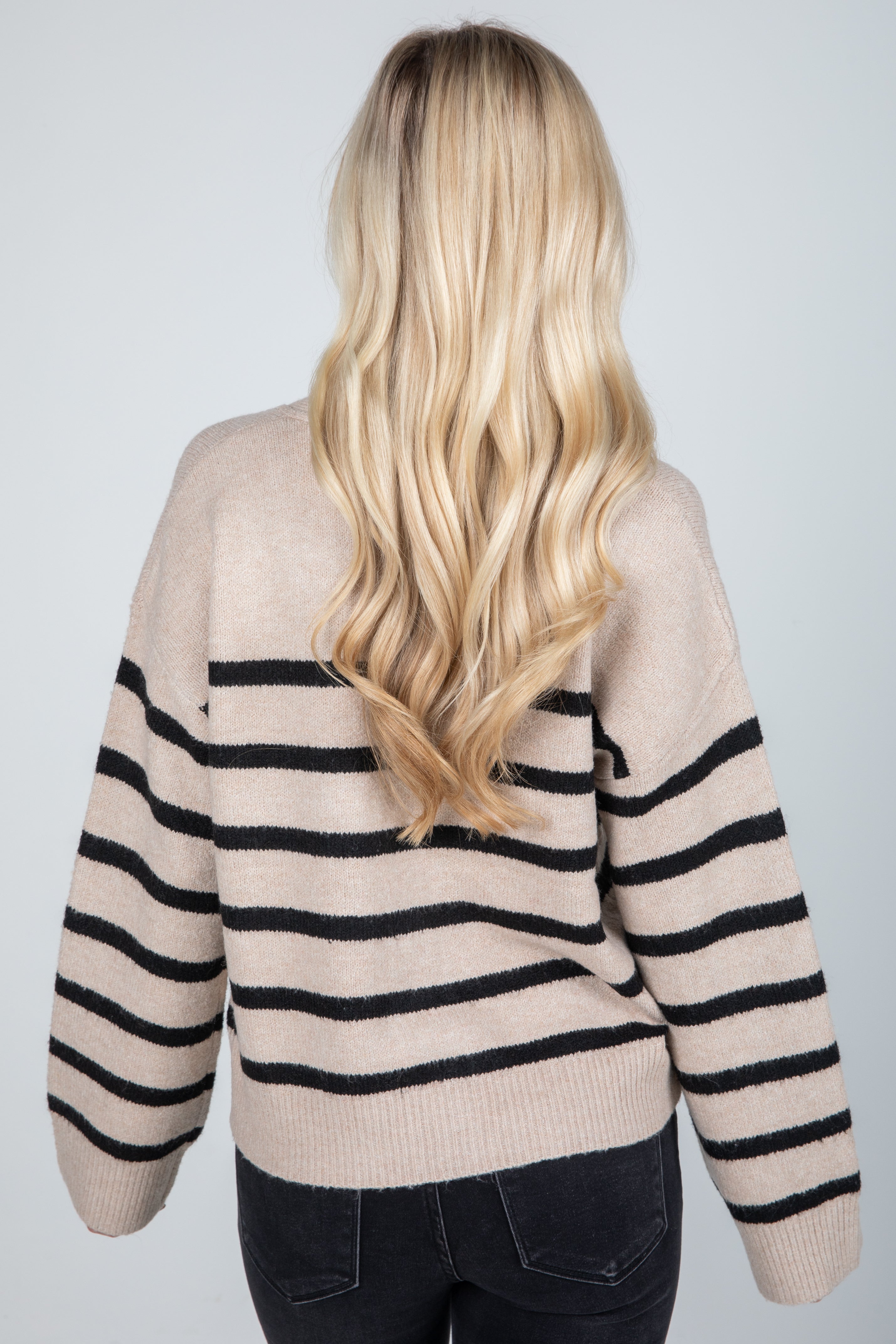 Person wearing a beige sweater with black stripes from behind on a light gray background