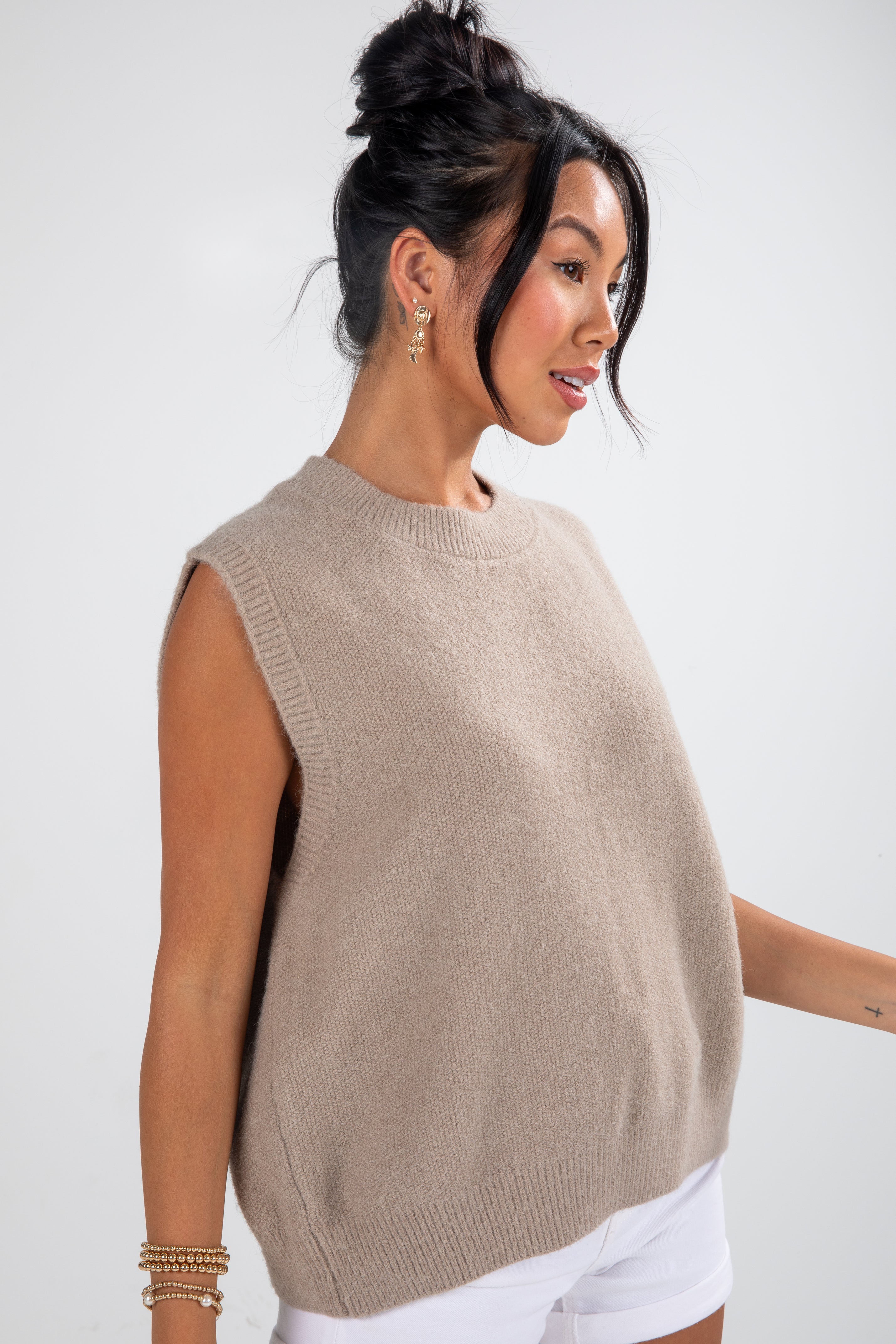 Woman wearing a beige sleeveless sweater against a white background