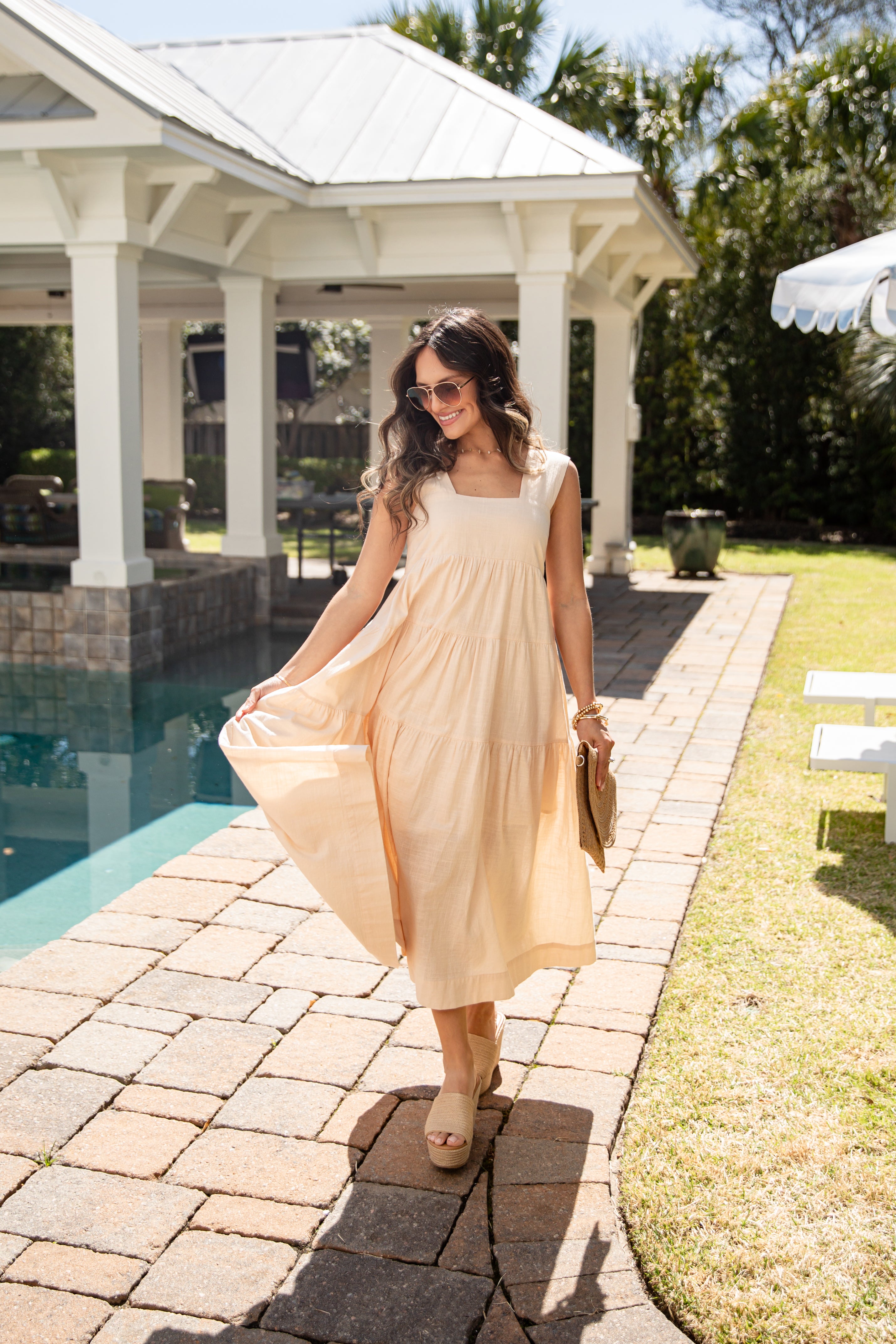 Woman in a beige dress standing by a poolside gazebo