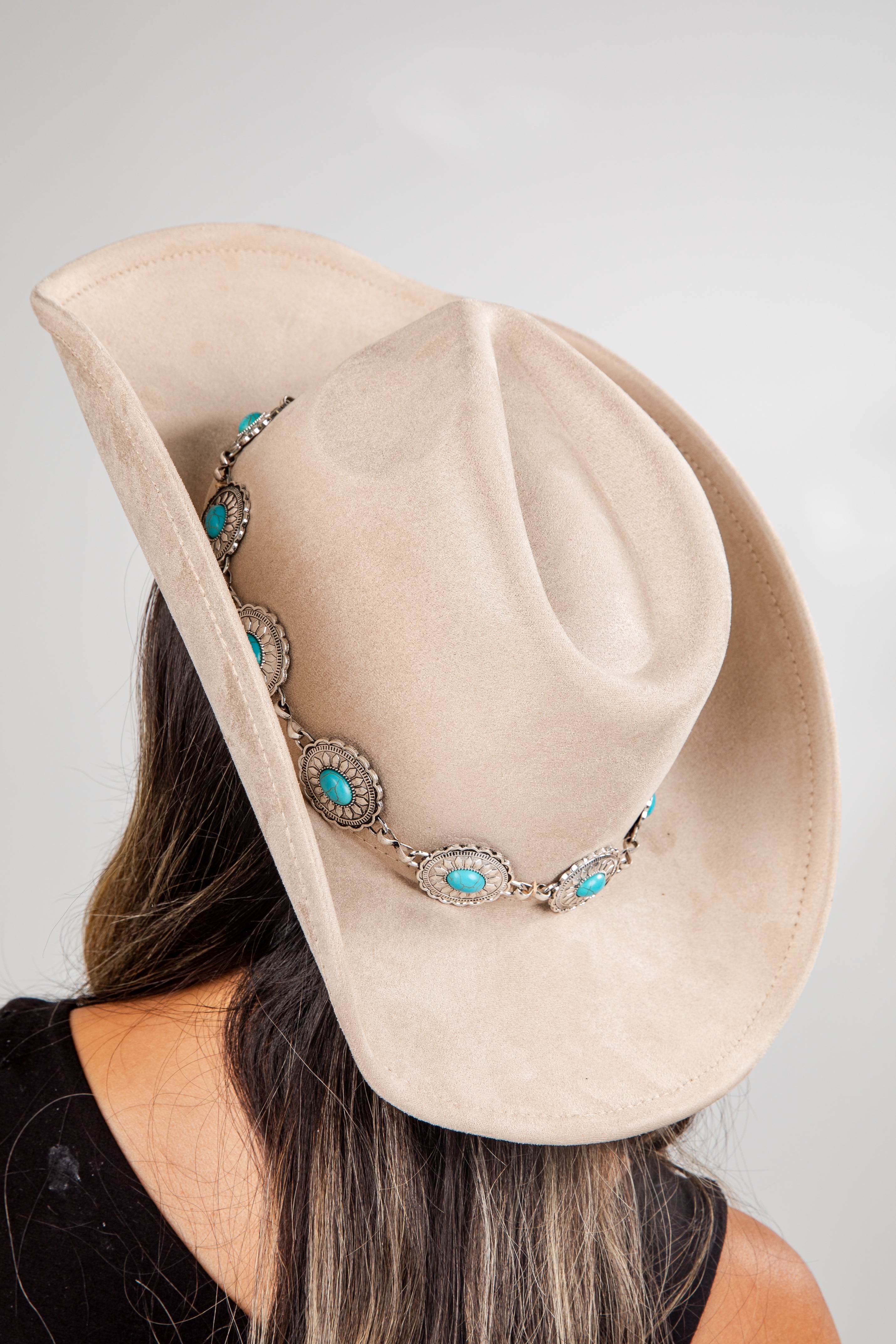 Beige cowboy hat with turquoise and silver accents worn by a person against a plain background