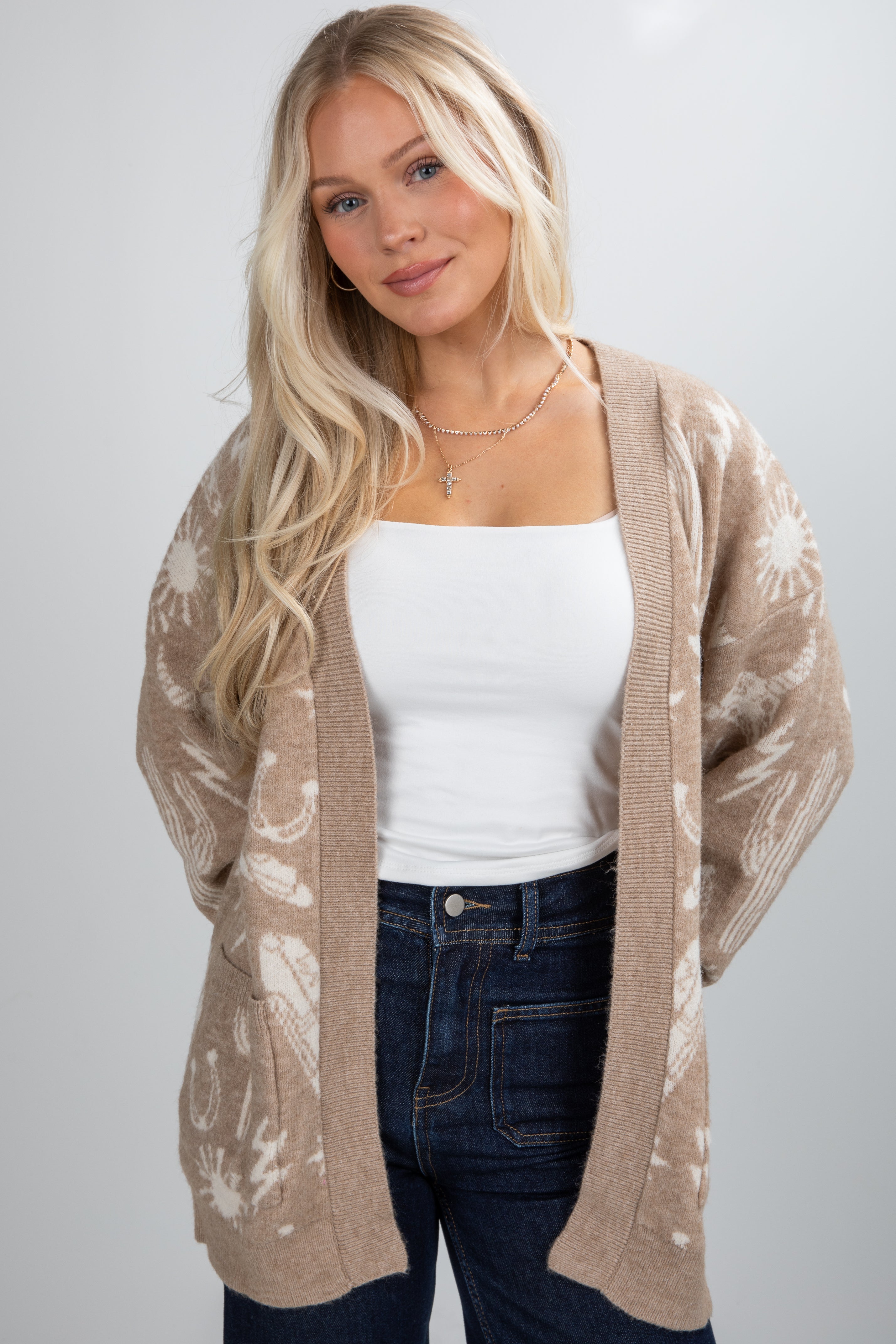 Woman wearing a beige patterned cardigan over a white top and jeans on a plain background