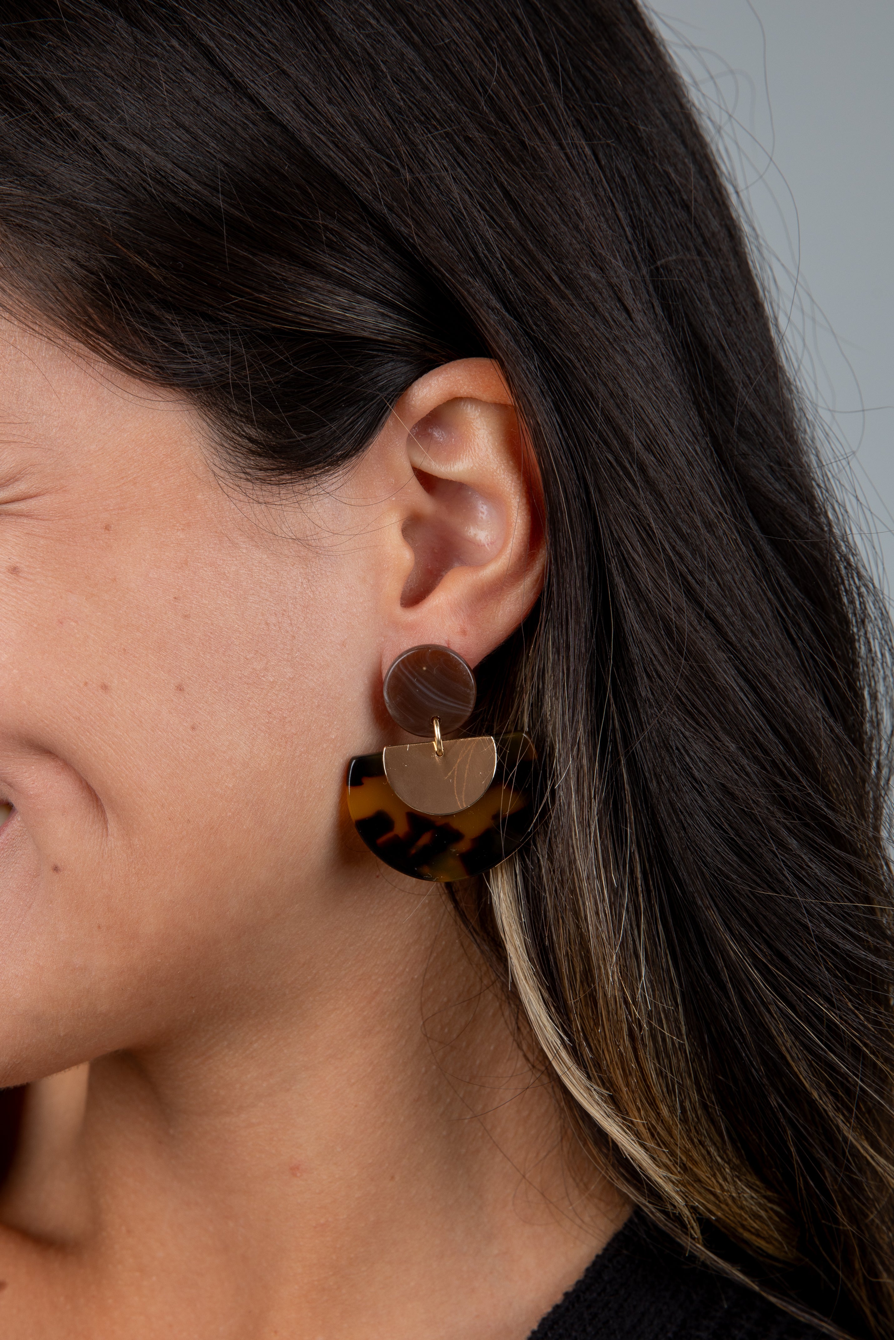 Close-up of a person wearing tortoiseshell heart-shaped earrings.