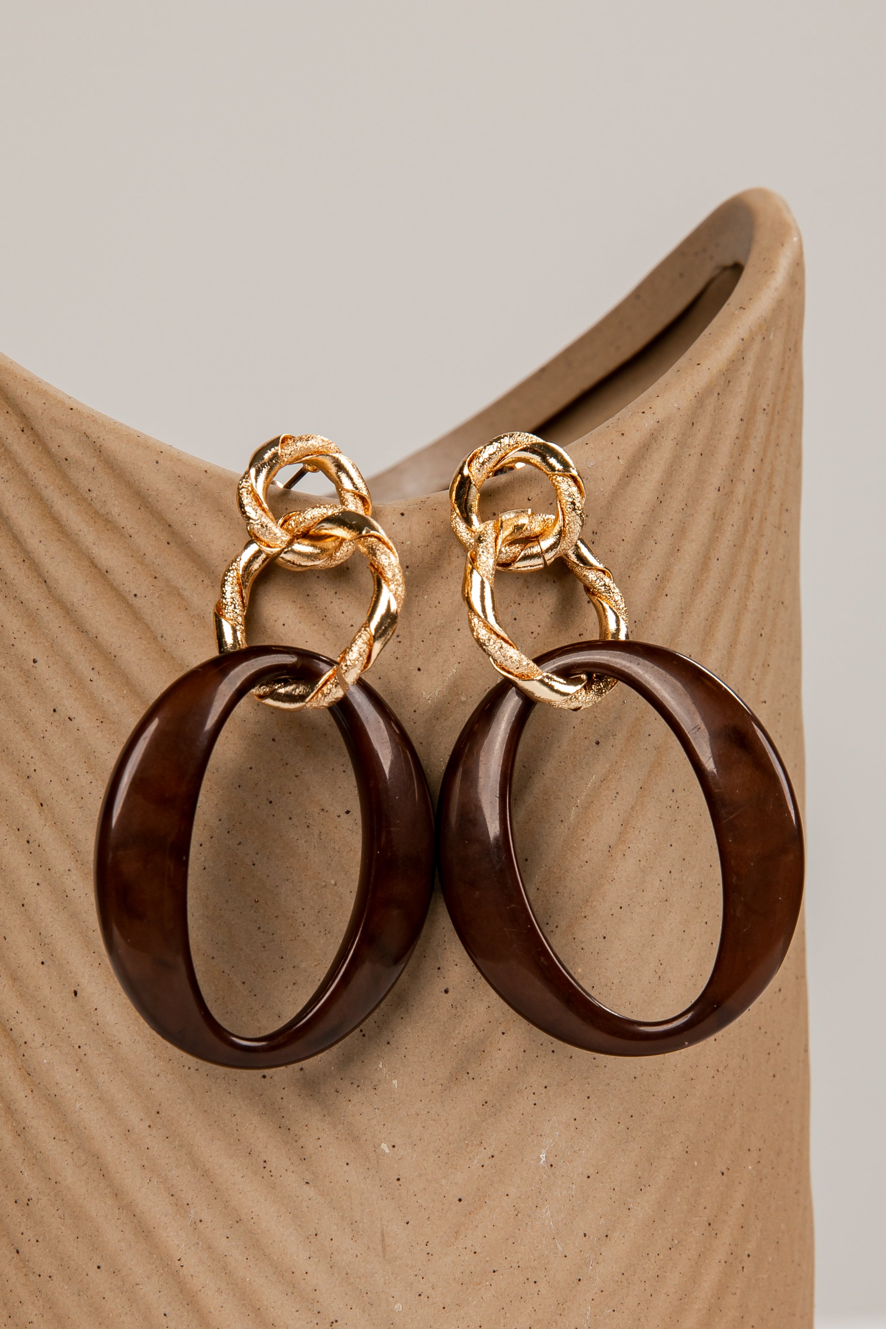 Pair of gold and brown hoop earrings on a wooden stand.