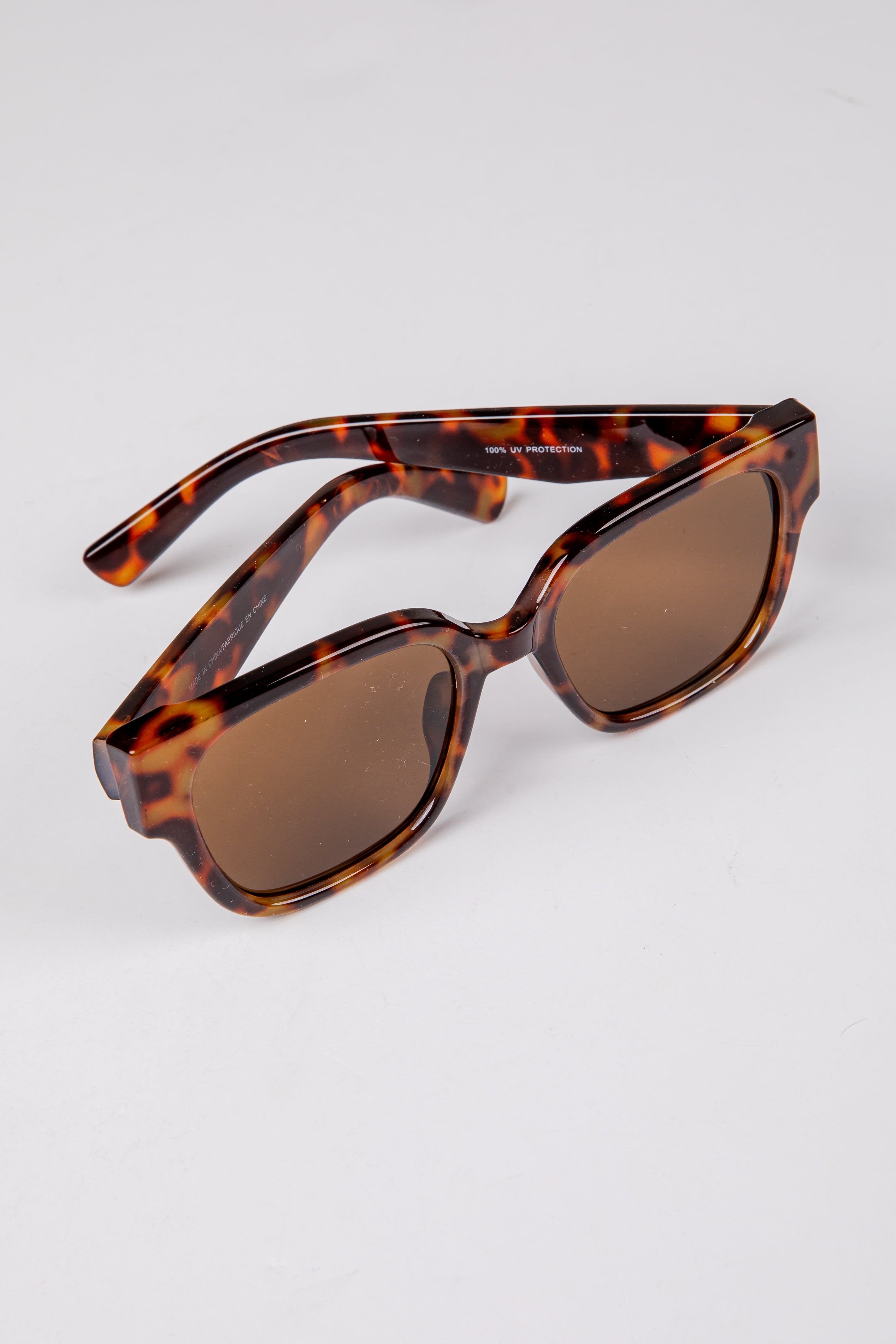 Sunglasses with tortoiseshell frame and brown lenses on a light gray background