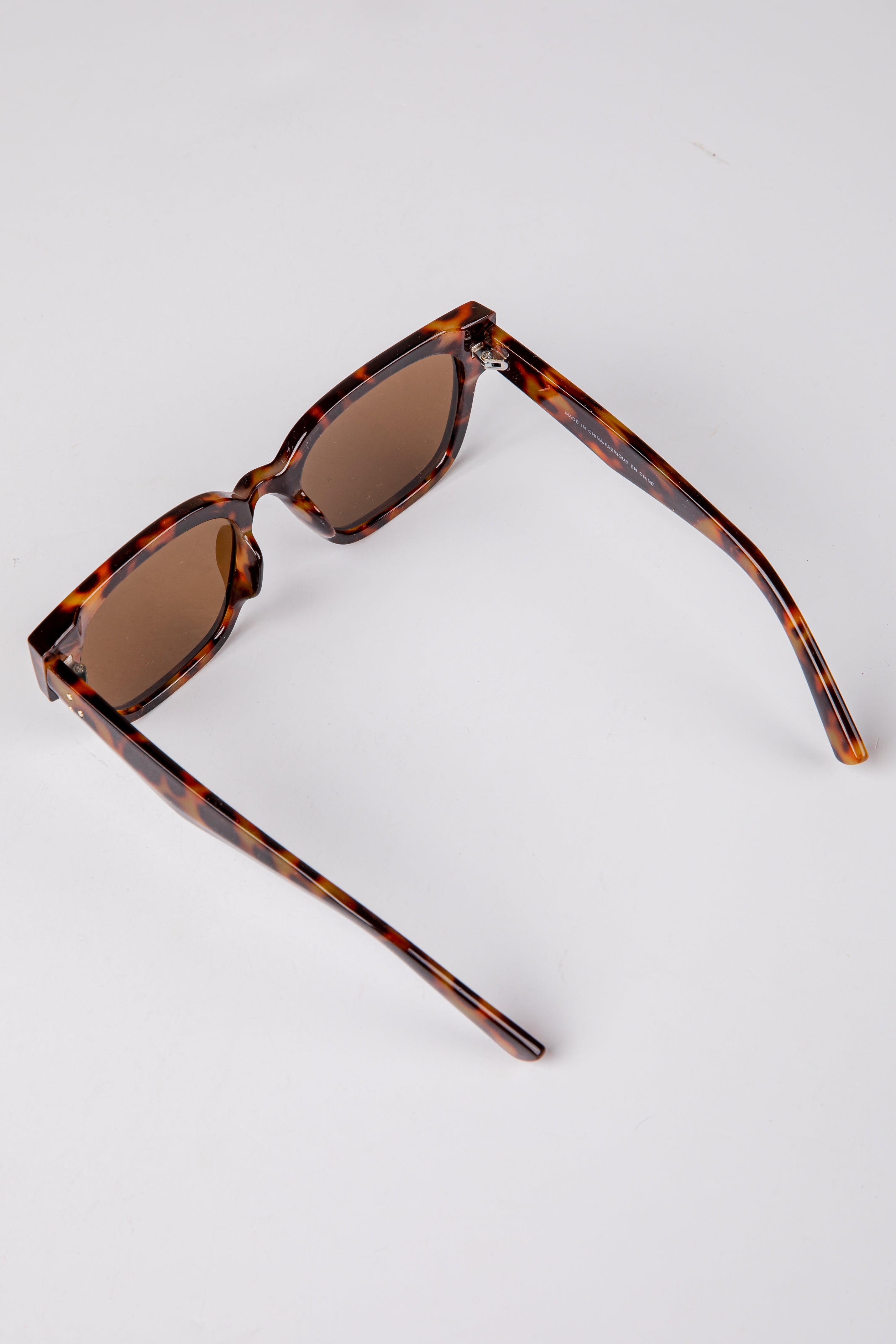Sunglasses with tortoiseshell frame and brown lenses on a light gray background