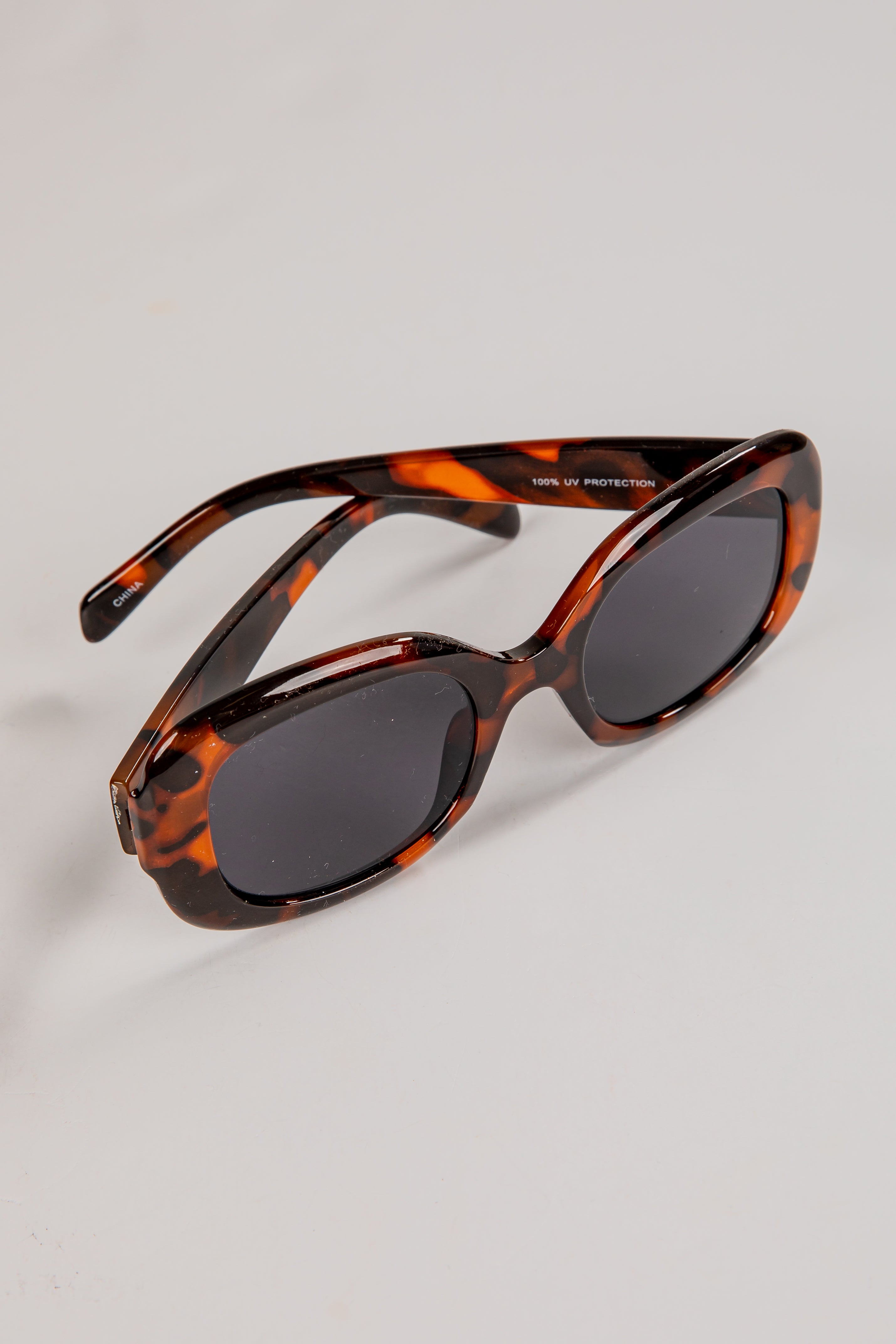 Sunglasses with tortoiseshell frame and dark lenses on a light gray background