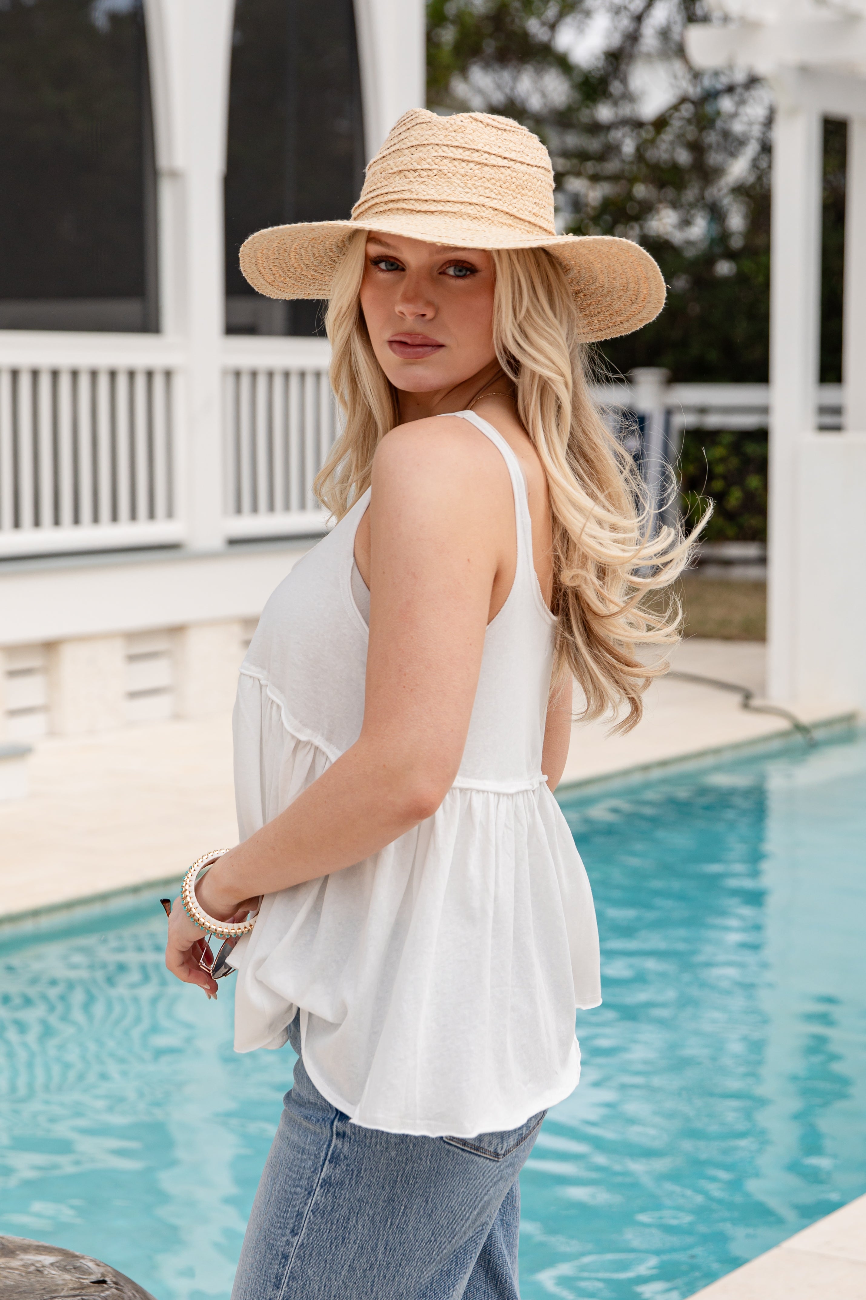 Woman wearing a white top and straw hat by a poolside.