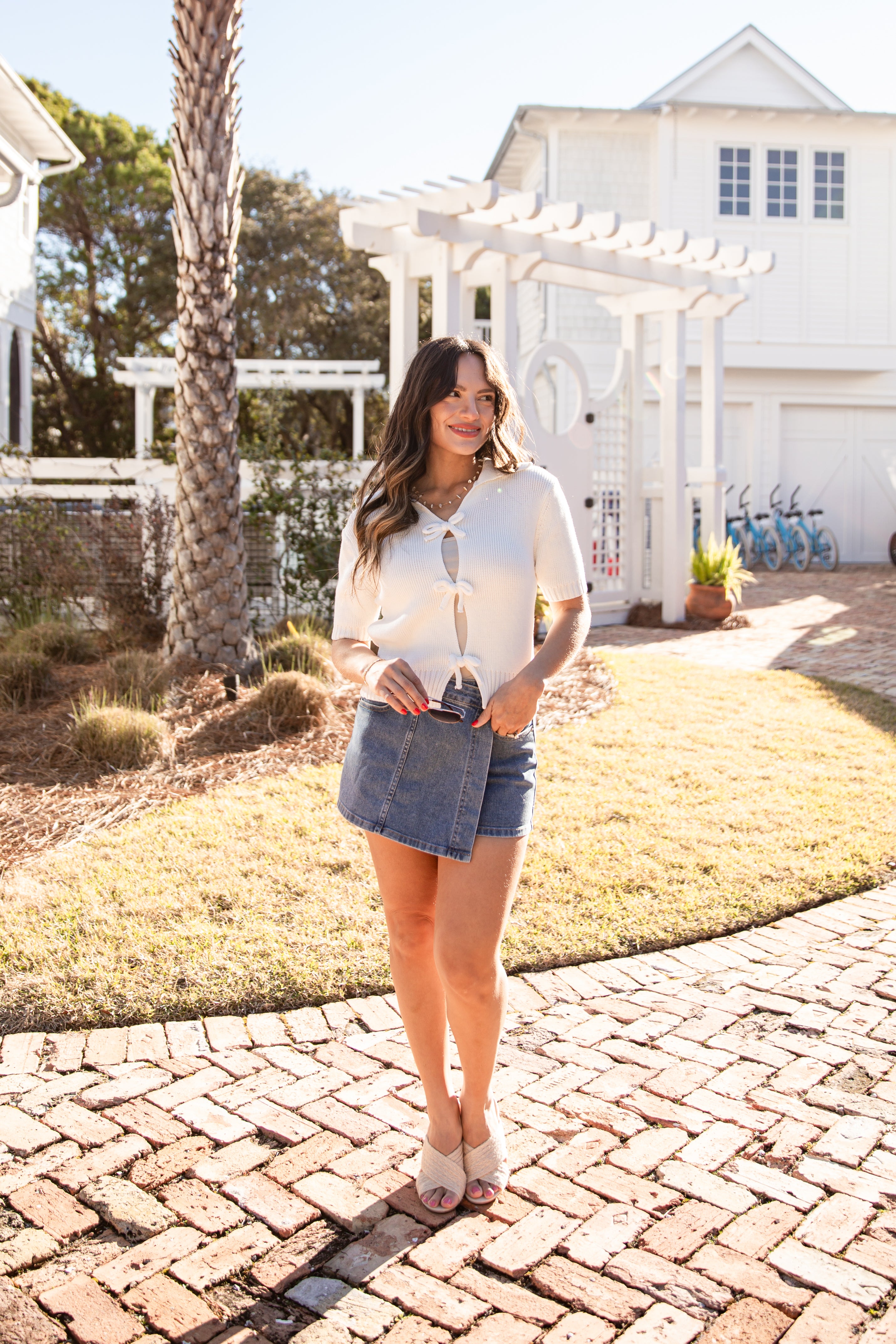Woman standing on a brick path in a garden with a white building and palm tree in the background