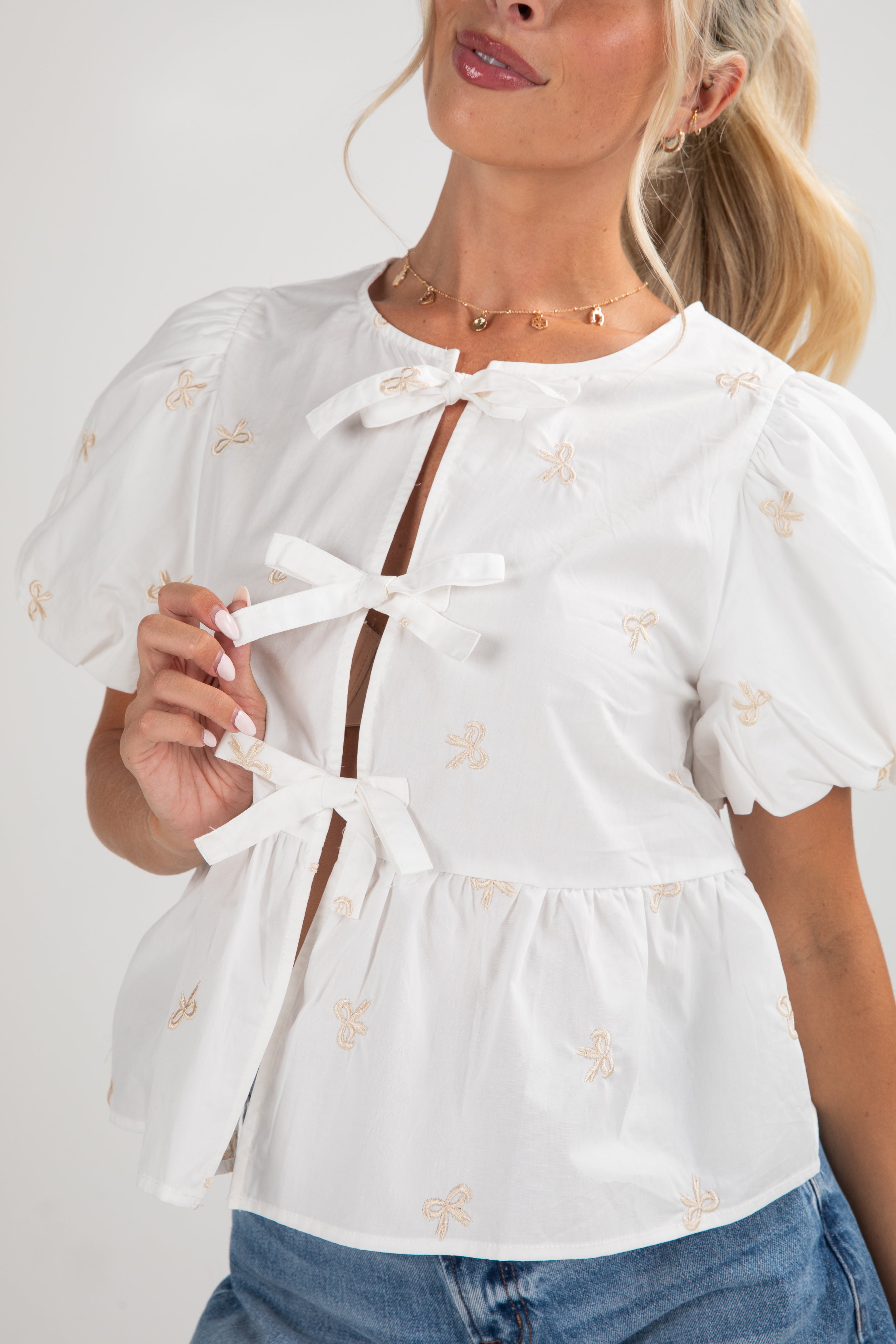 Woman wearing a white blouse with bow details and blue jeans on a plain background