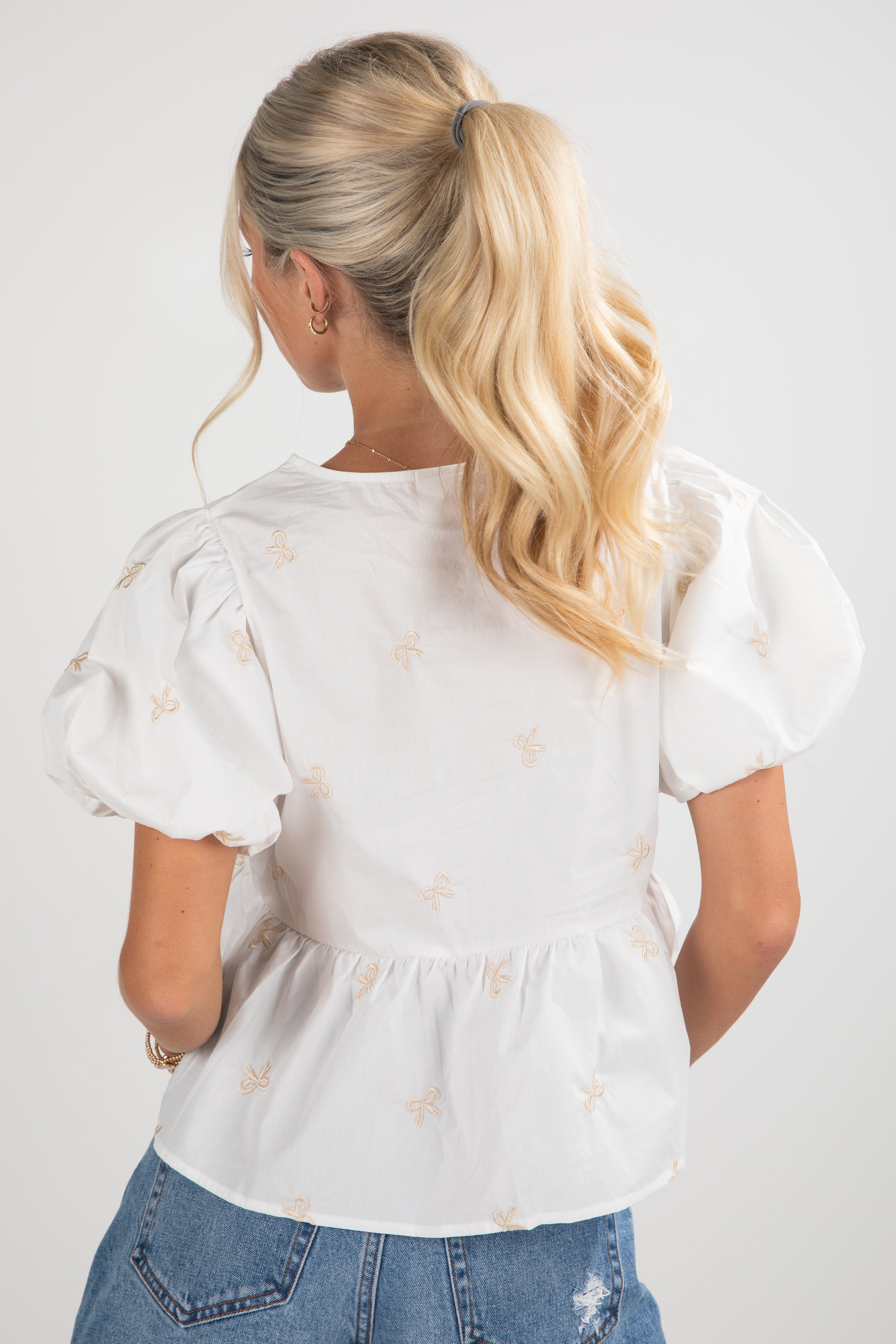 Woman wearing a white blouse with puff sleeves and star patterns, standing against a plain background.