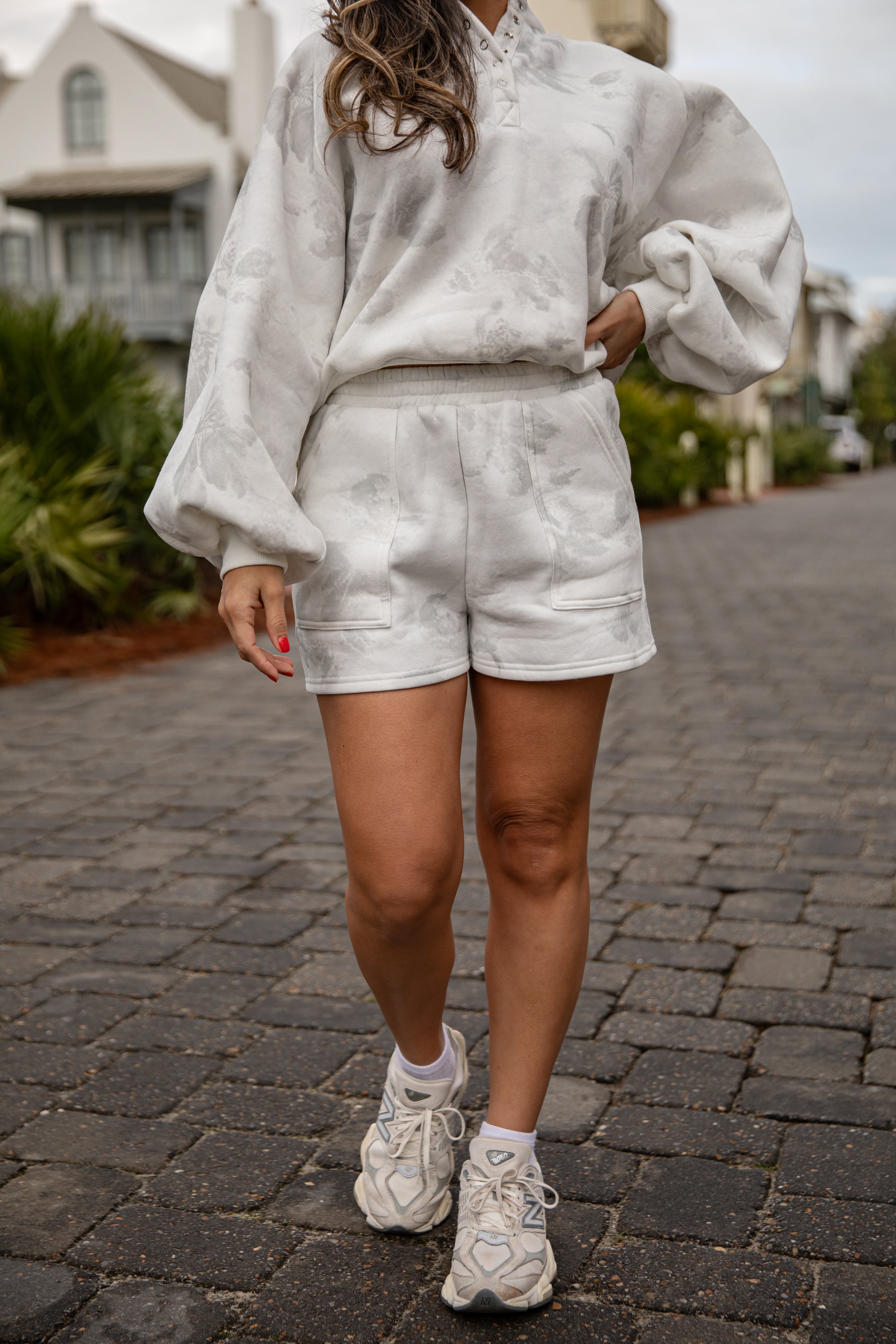 Person wearing a light gray outfit with shorts and sneakers on a paved walkway.