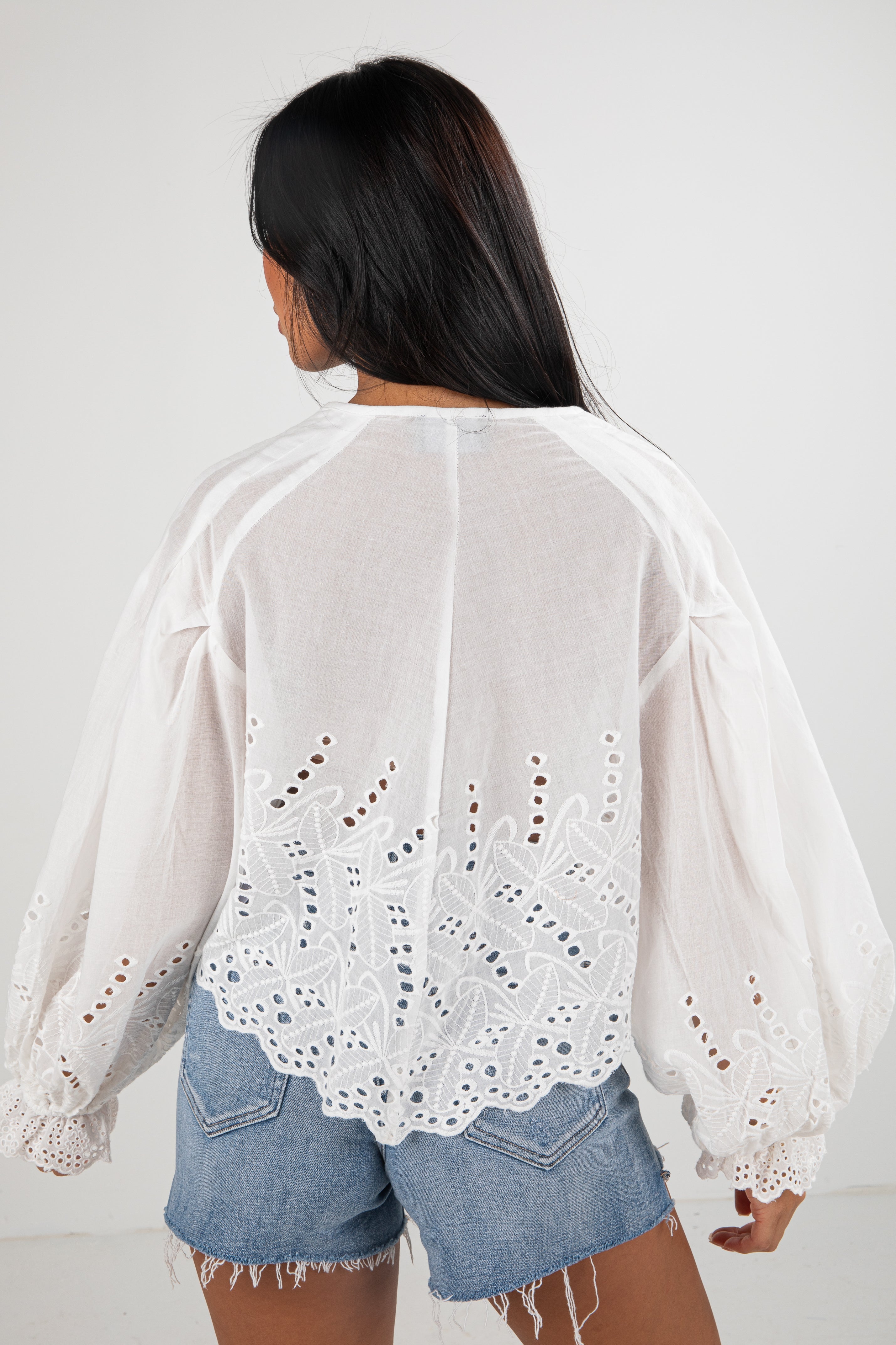 Person wearing a white lace top and denim shorts on a plain background