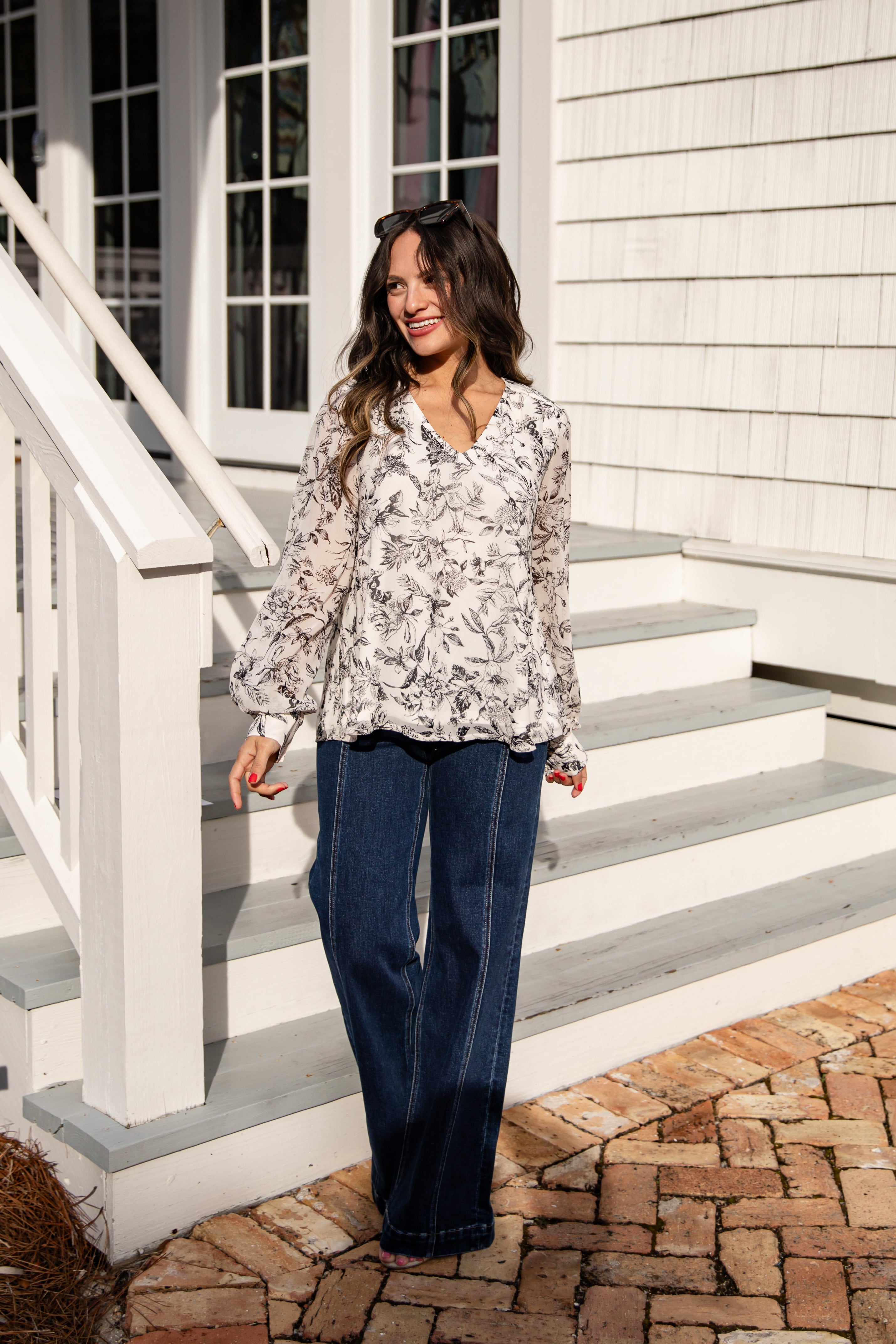 Woman standing on a set of stairs wearing a floral blouse and blue jeans.