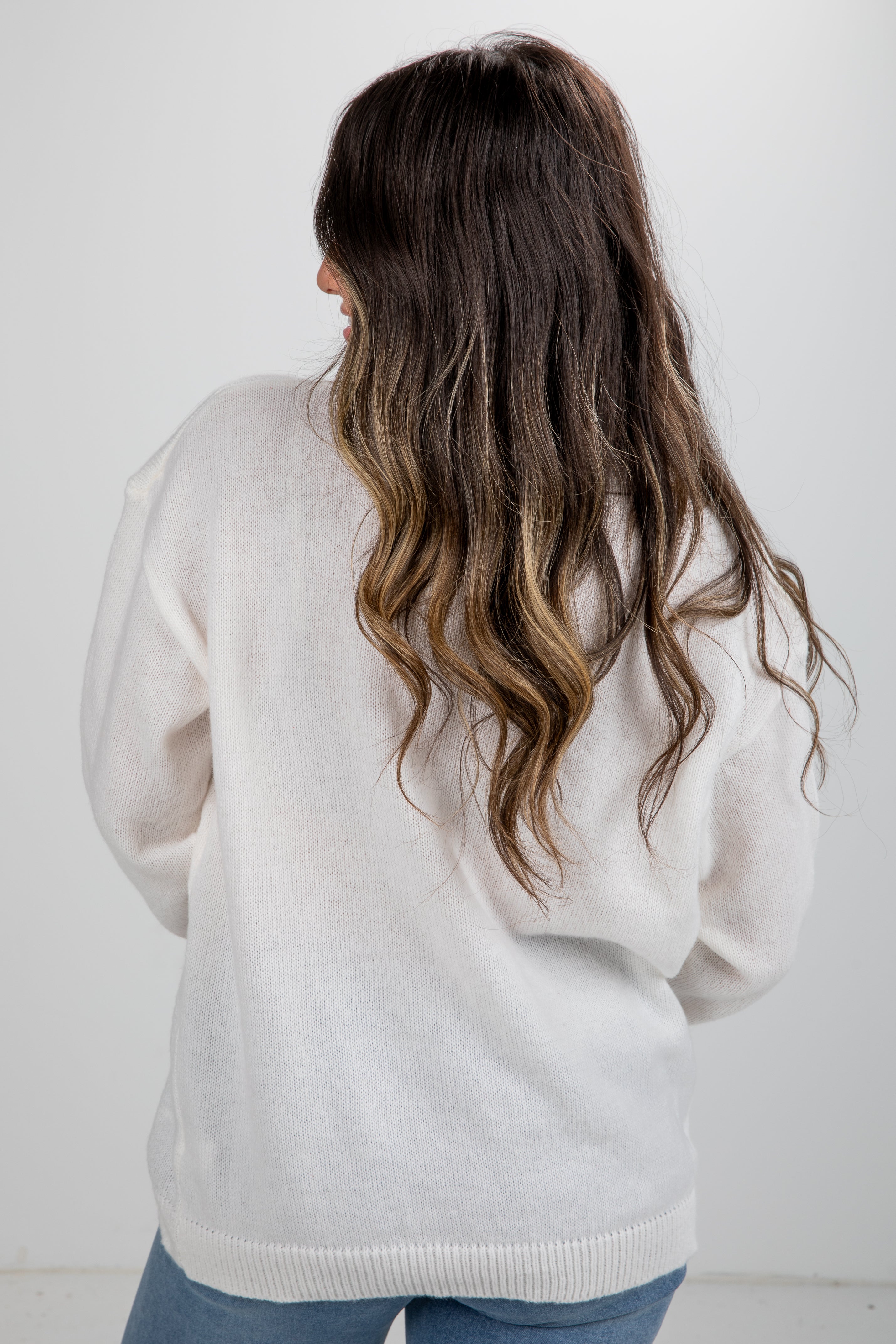 Person wearing a light gray sweater with long, wavy hair on a white background
