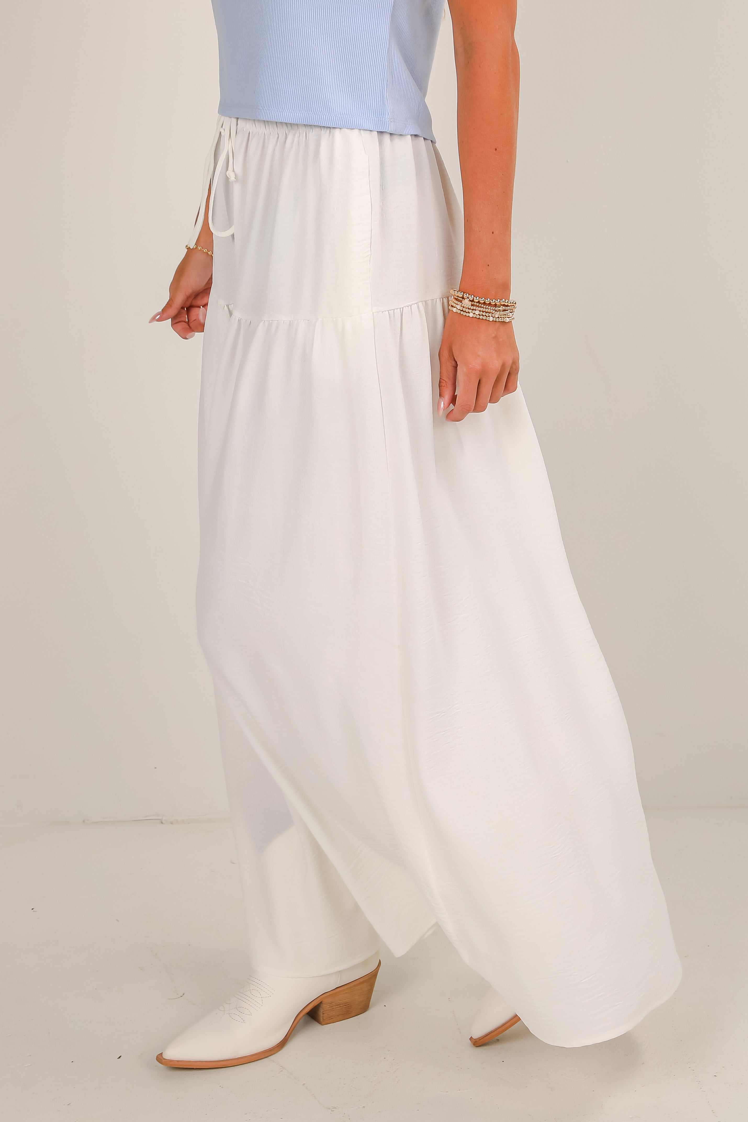 Person wearing a light blue top and white wide-leg pants on a plain background