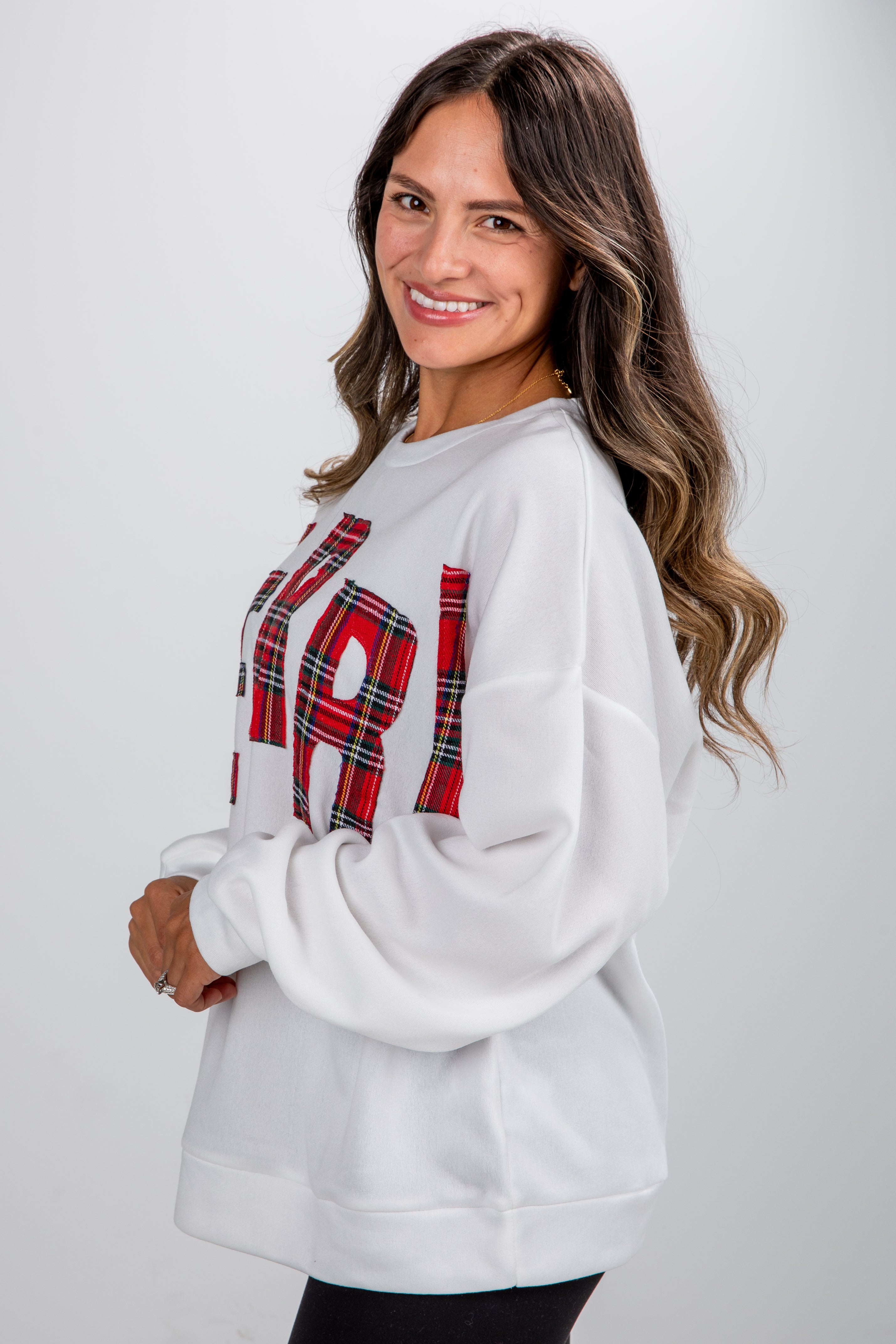 Woman wearing a white sweatshirt with plaid lettering on a plain background