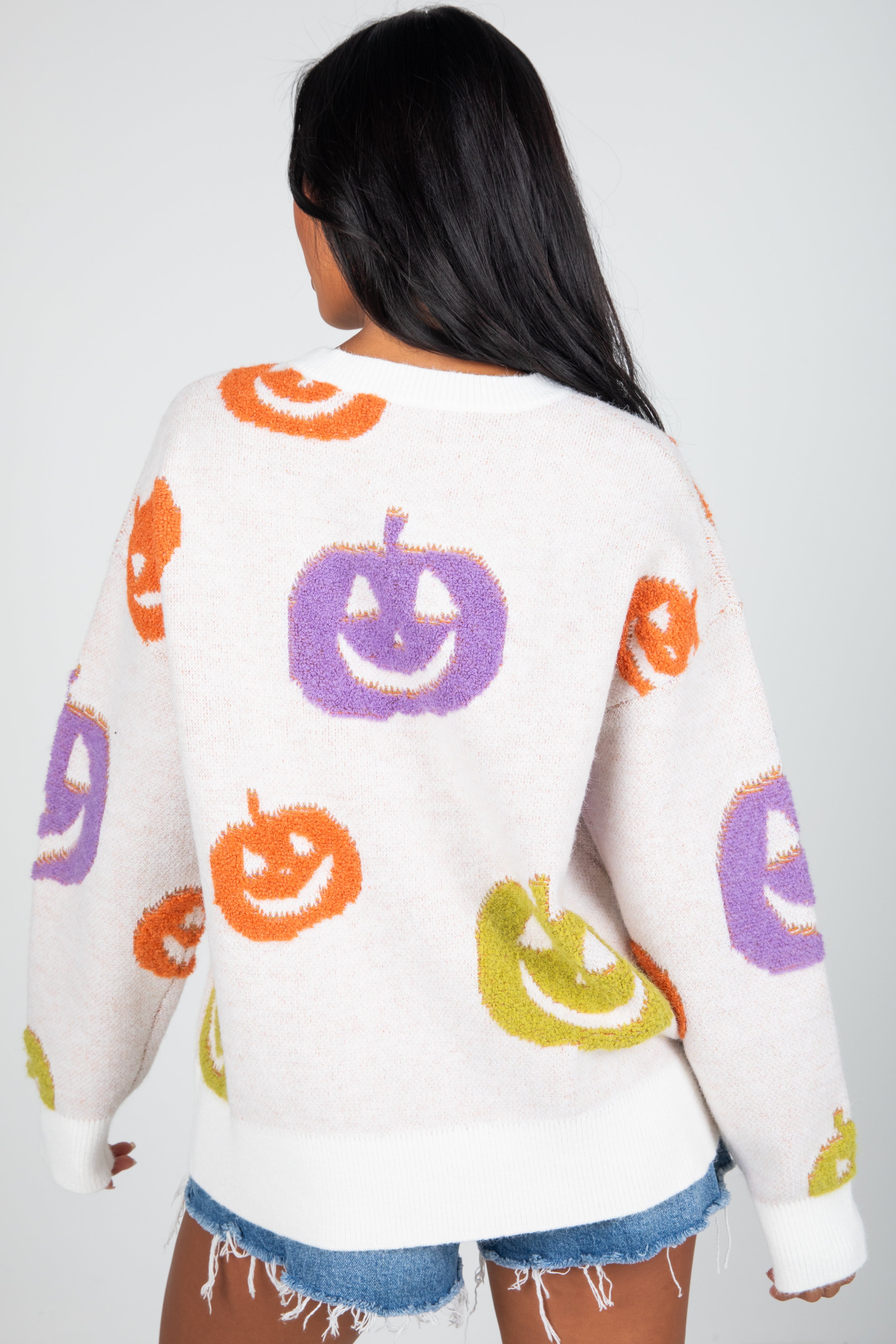Person wearing a sweater with colorful pumpkin designs on a plain background