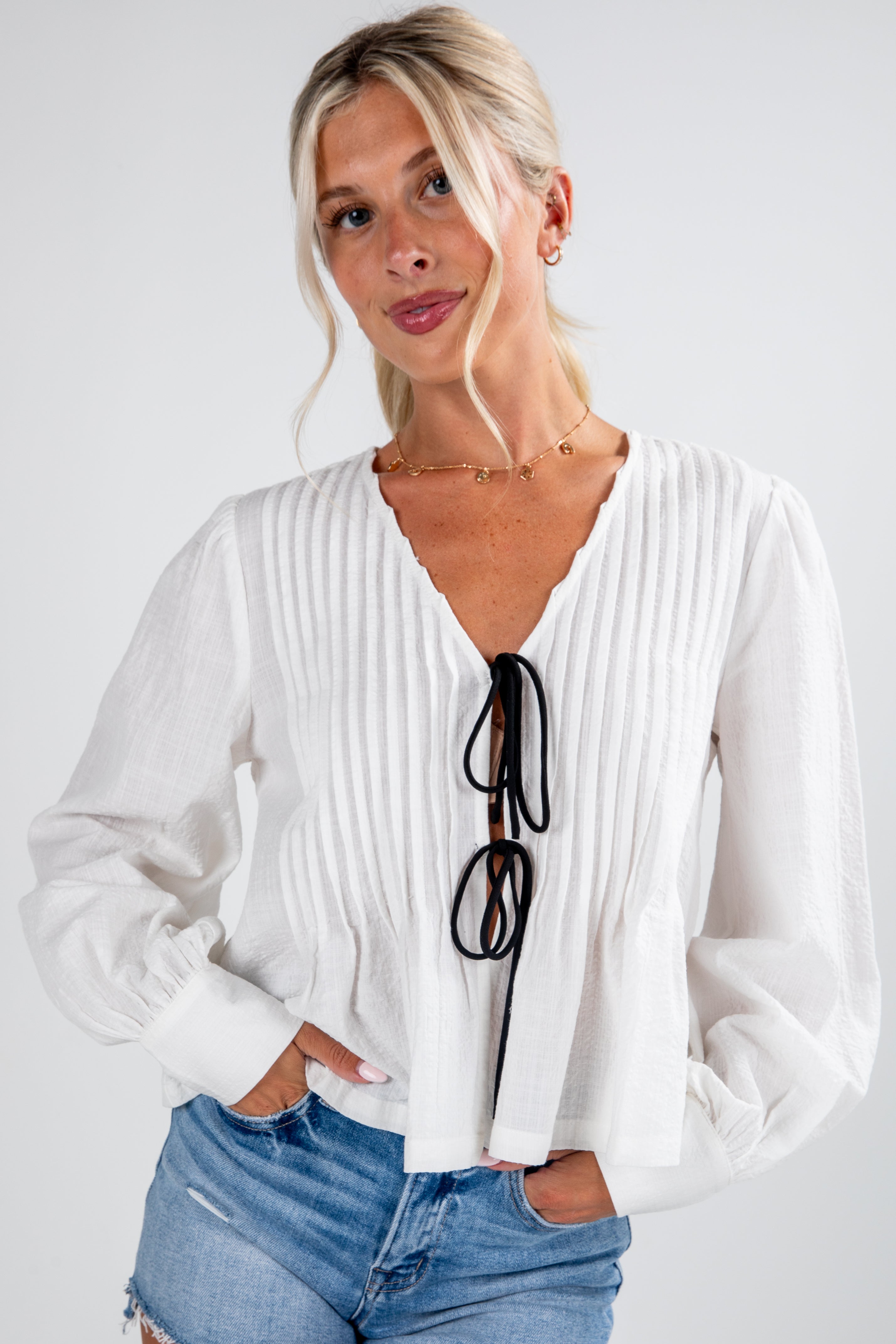 Woman wearing a white blouse with a deep neckline and blue jeans on a plain background