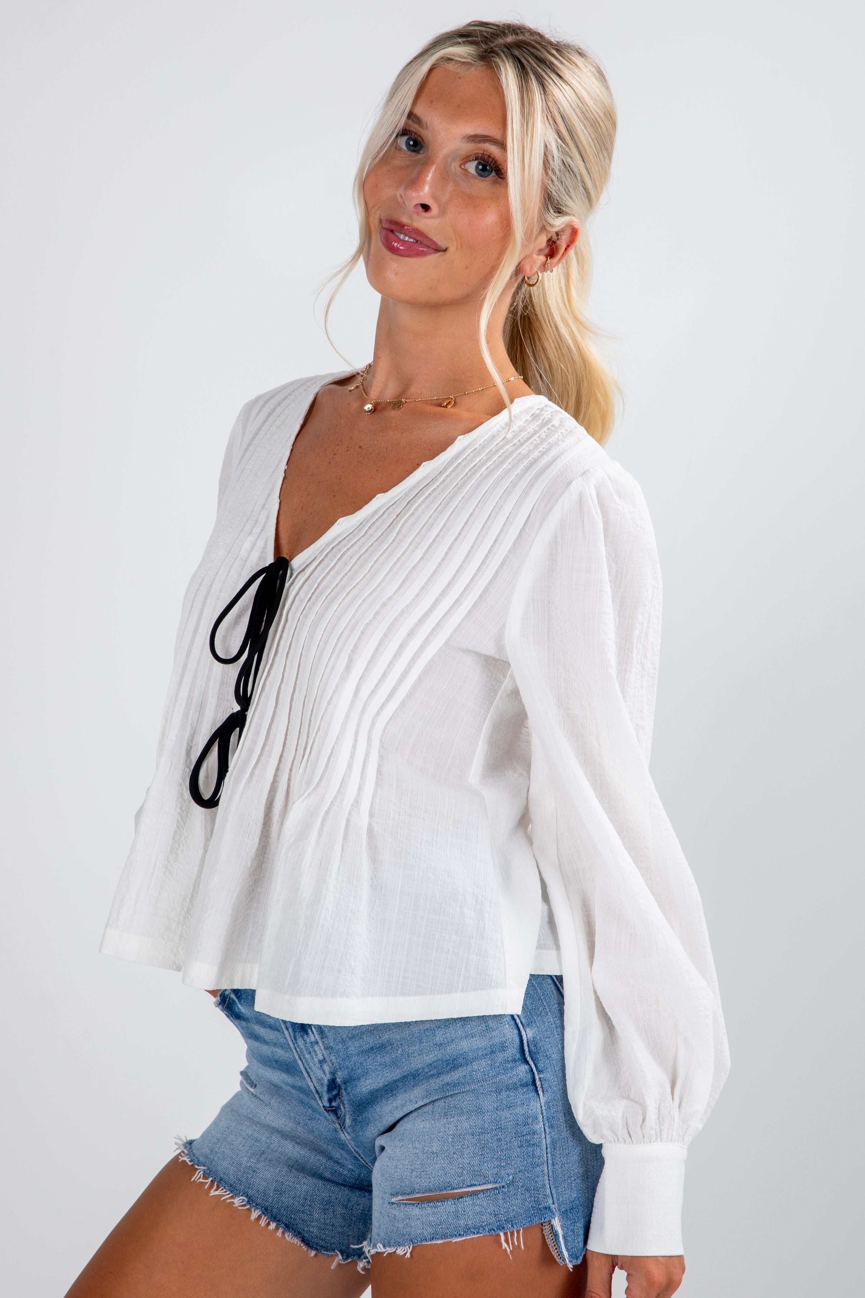 Woman wearing a white blouse with a black tie and denim shorts on a plain background