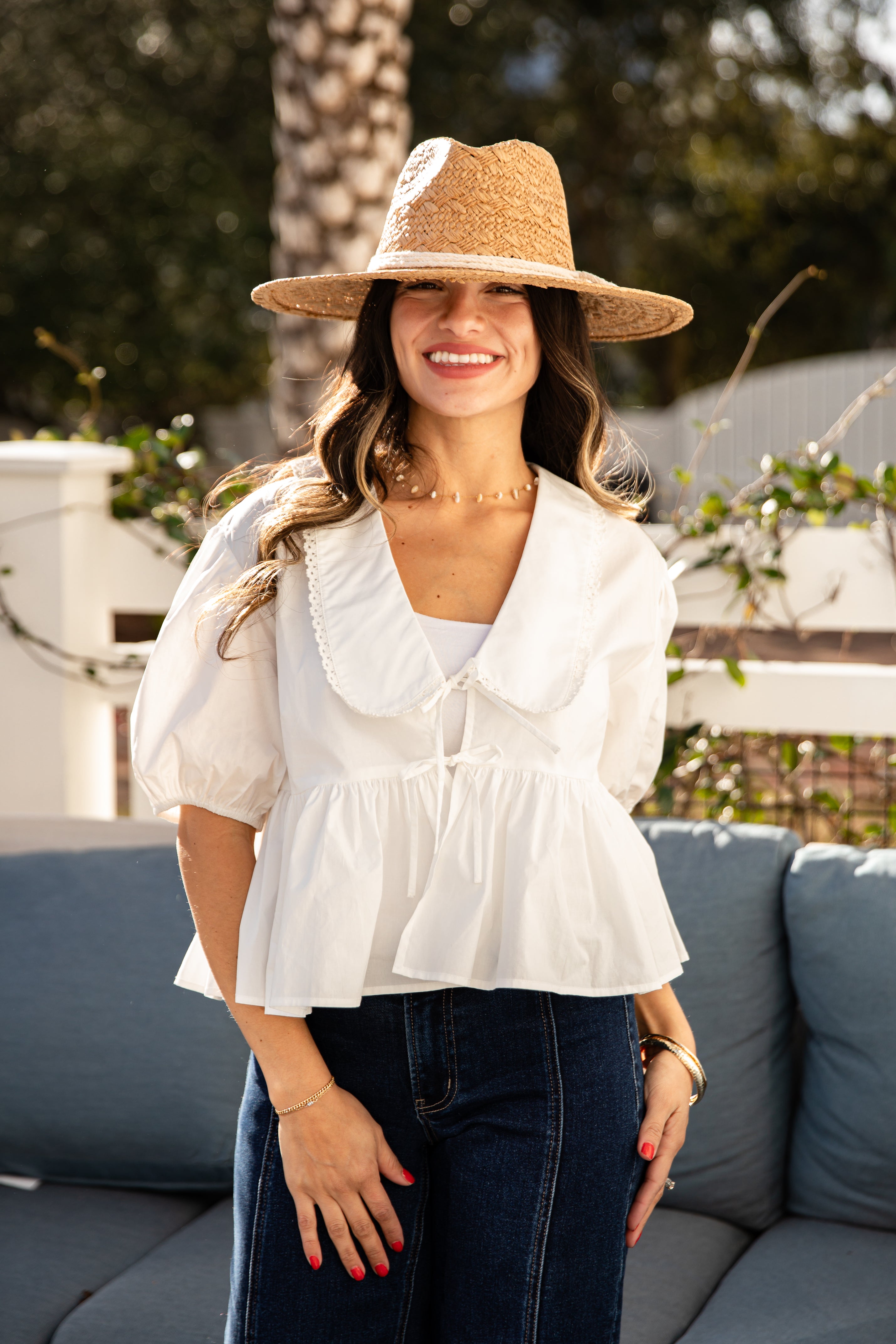 Woman wearing a white blouse, blue jeans, and a straw hat outdoors.