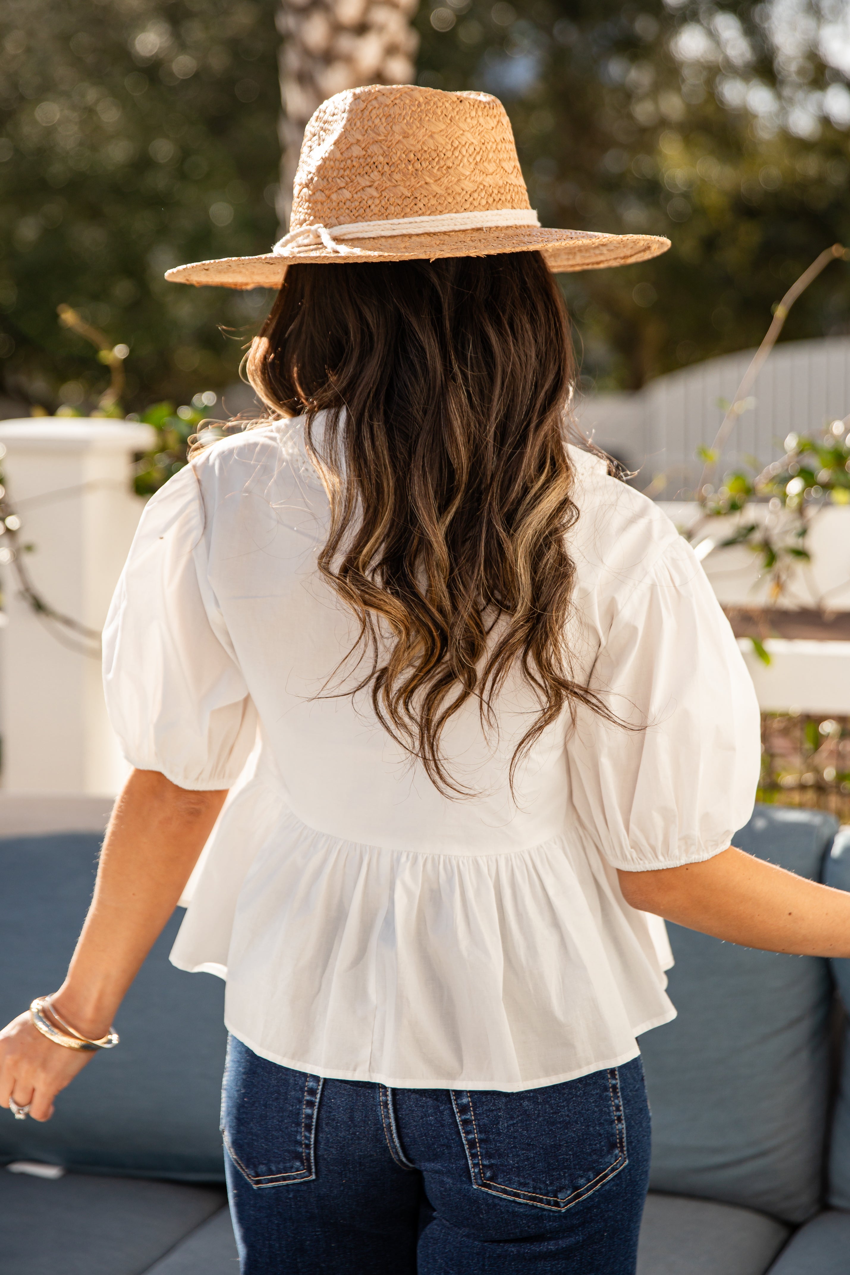 Person wearing a white blouse and straw hat in an outdoor setting