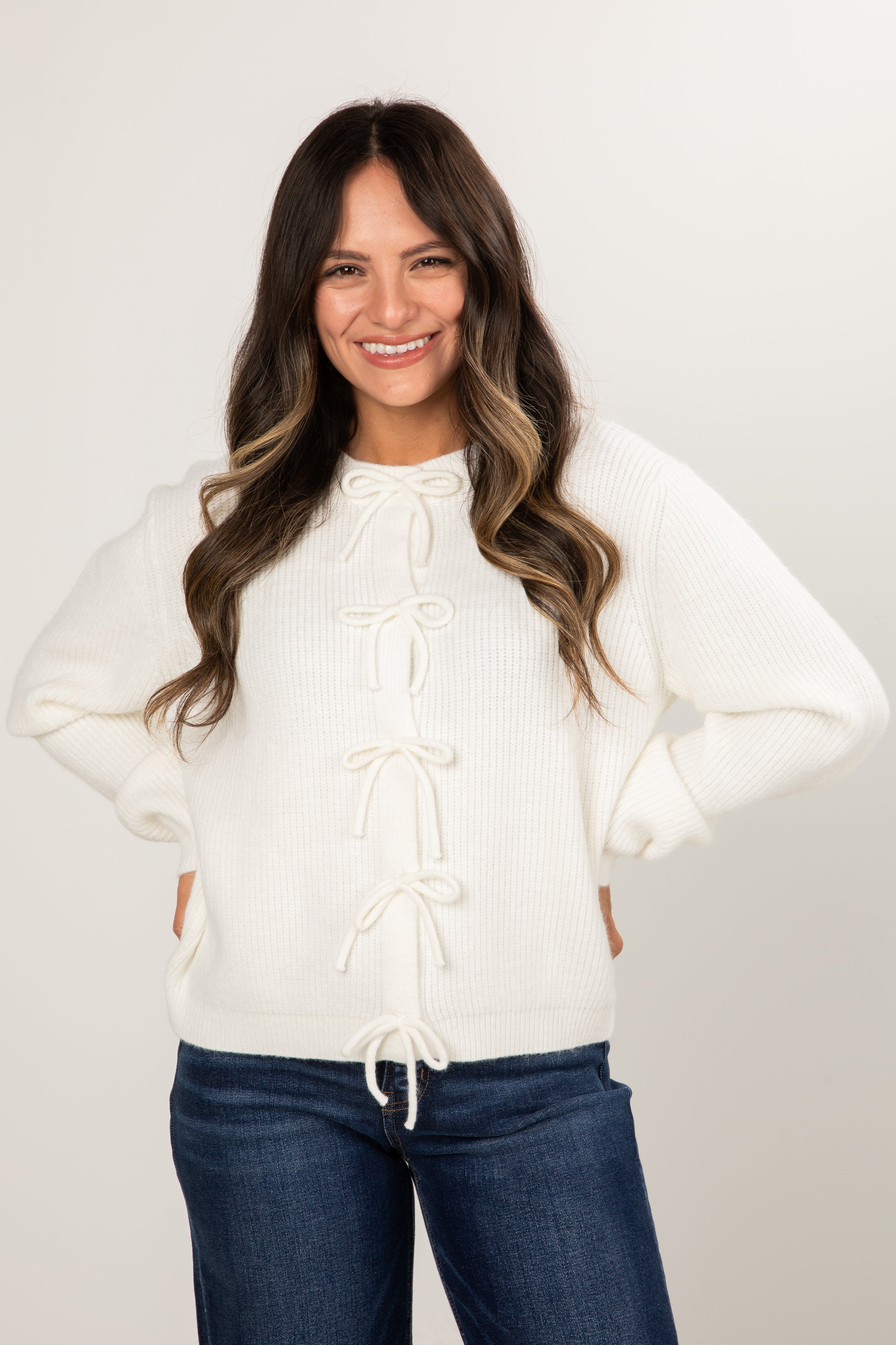 Woman wearing a white sweater with lace-up front design against a plain background