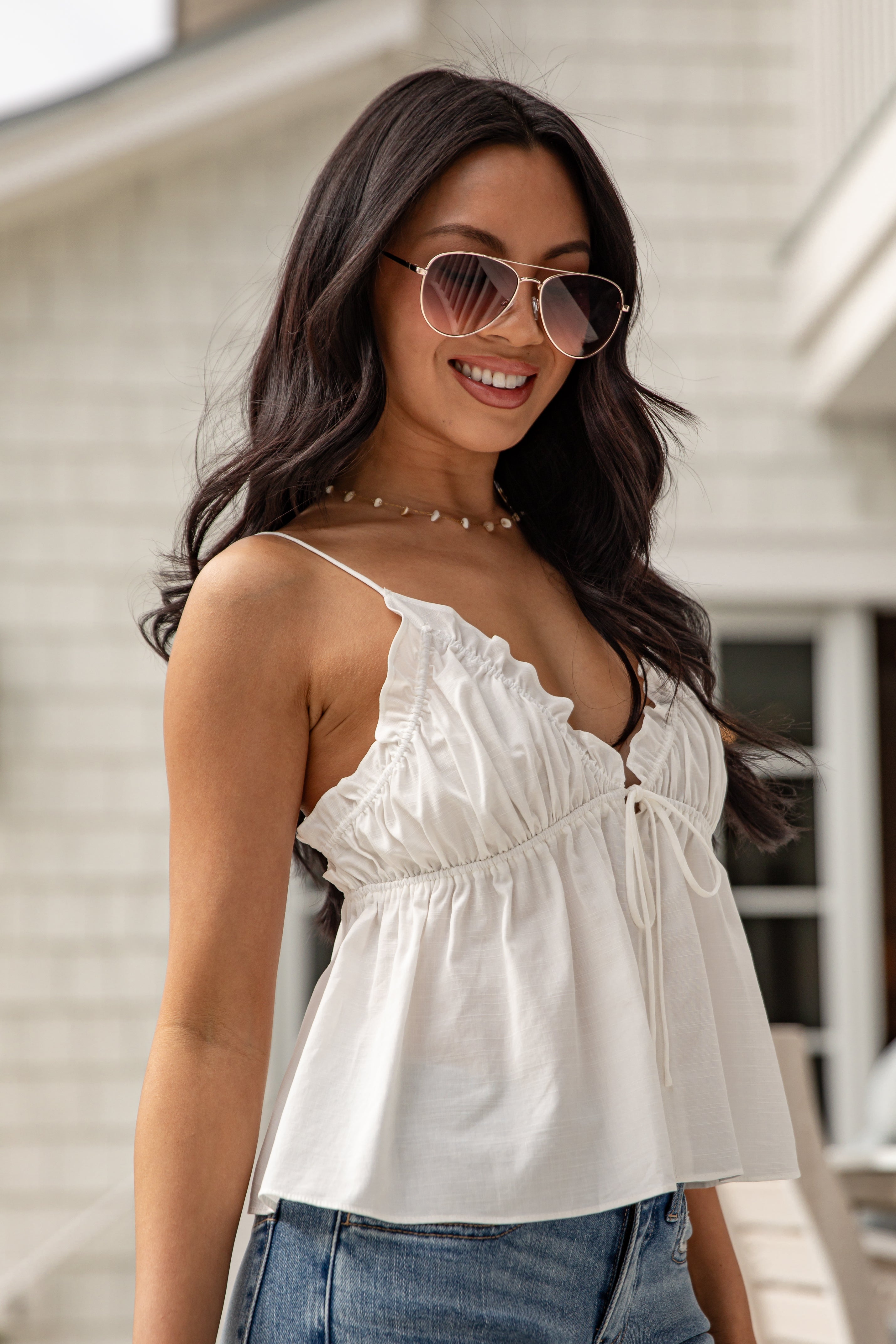 Woman wearing a white top and sunglasses with a blurred background