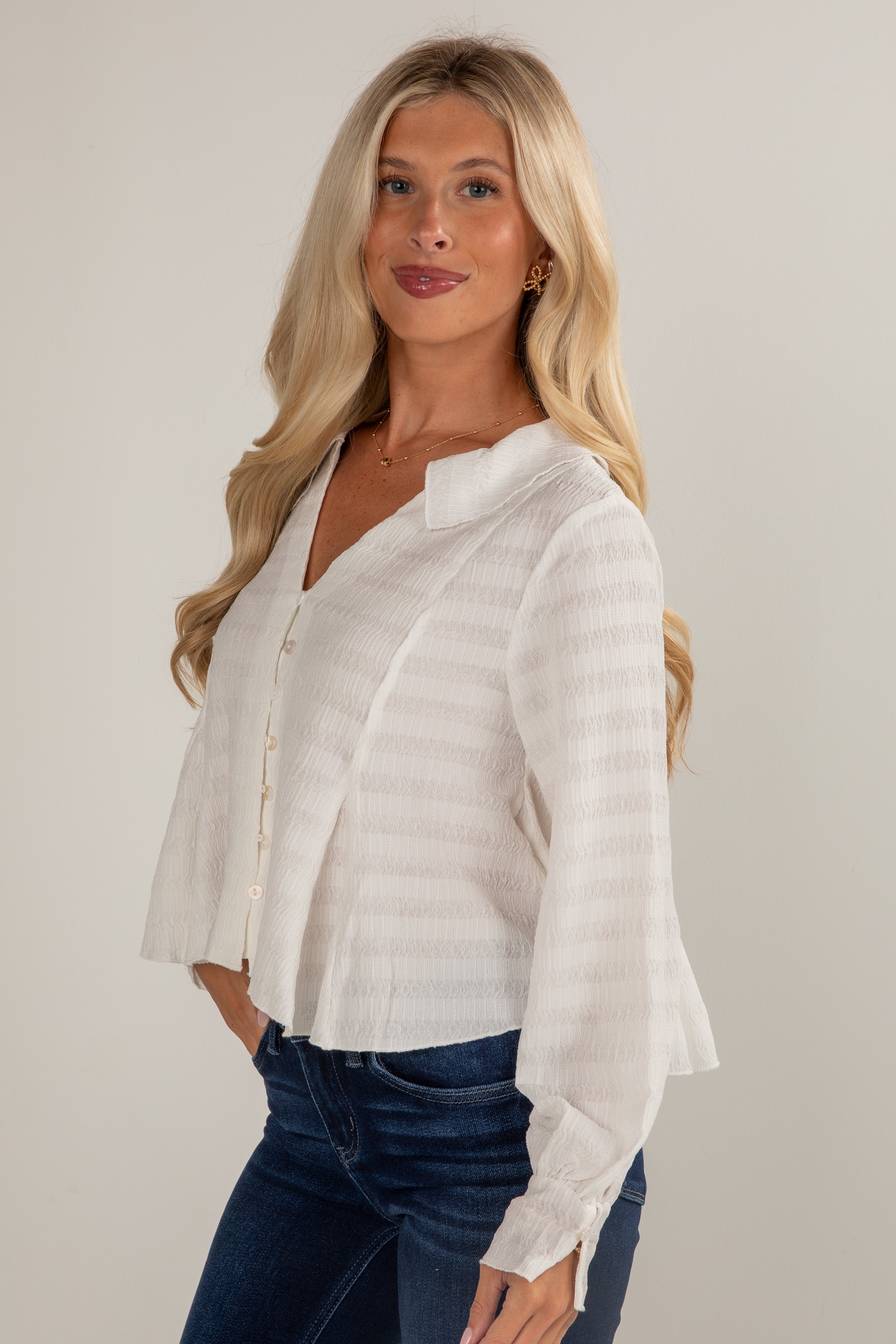 Woman wearing a white blouse and blue jeans against a plain background
