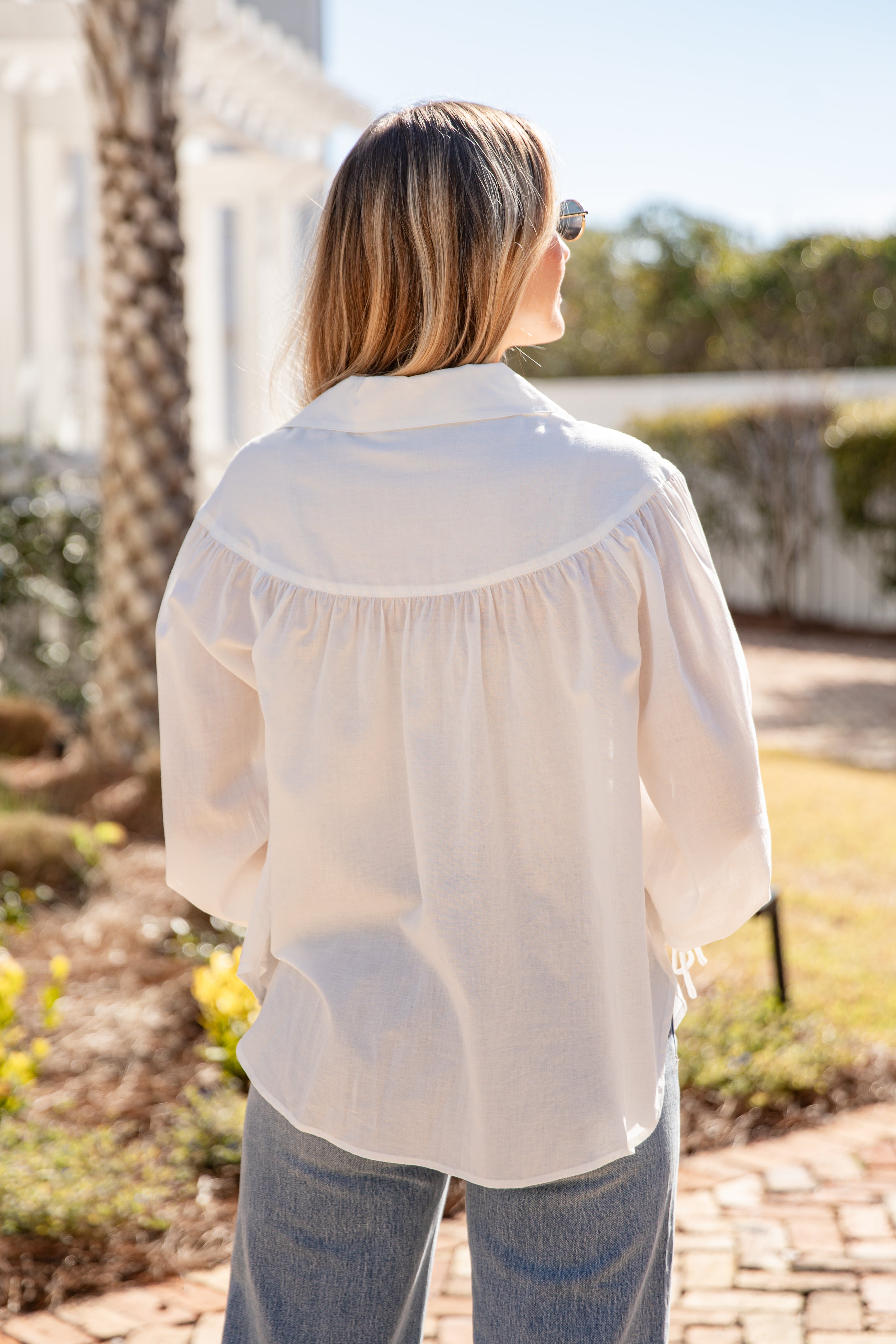 Woman wearing a white blouse outdoors with greenery in the background