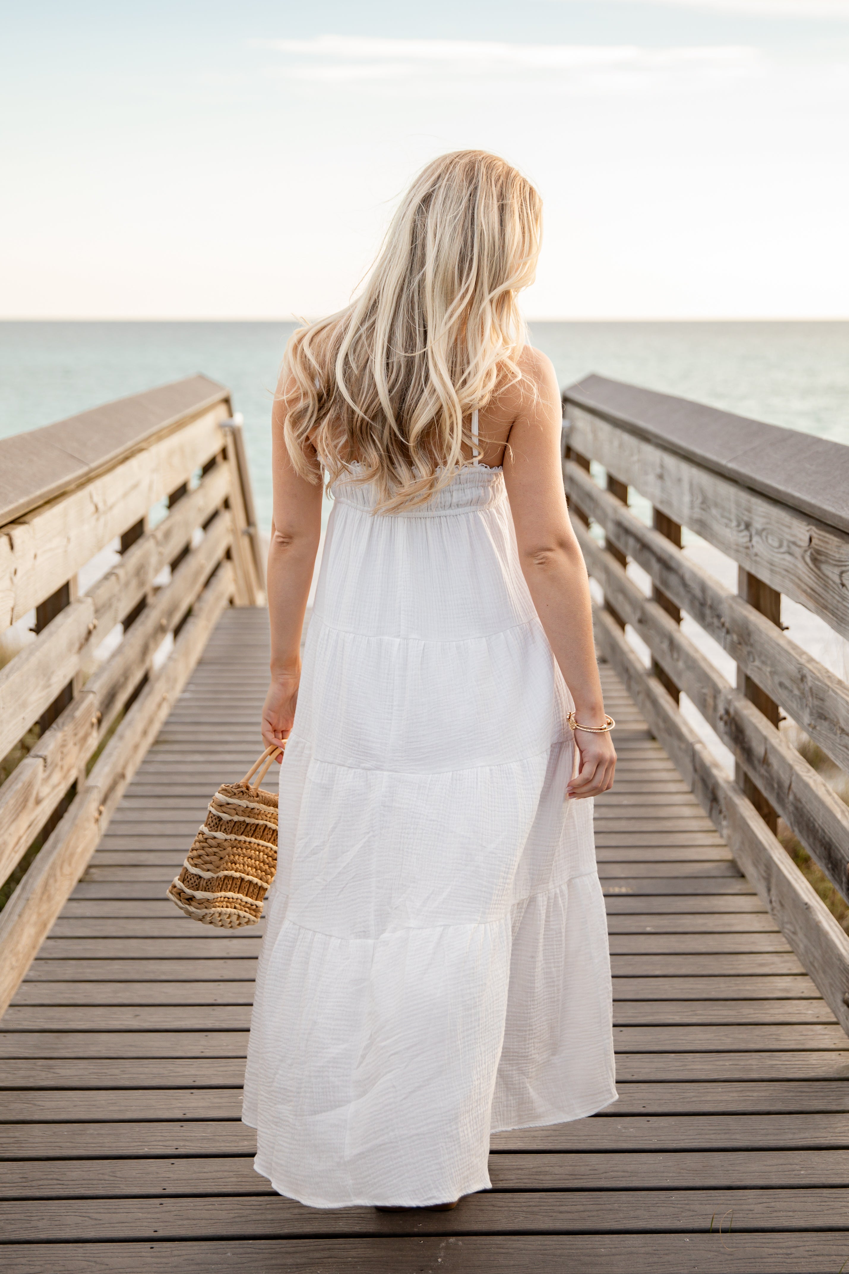 Woman in a white dress standing on a wooden pier by the water.