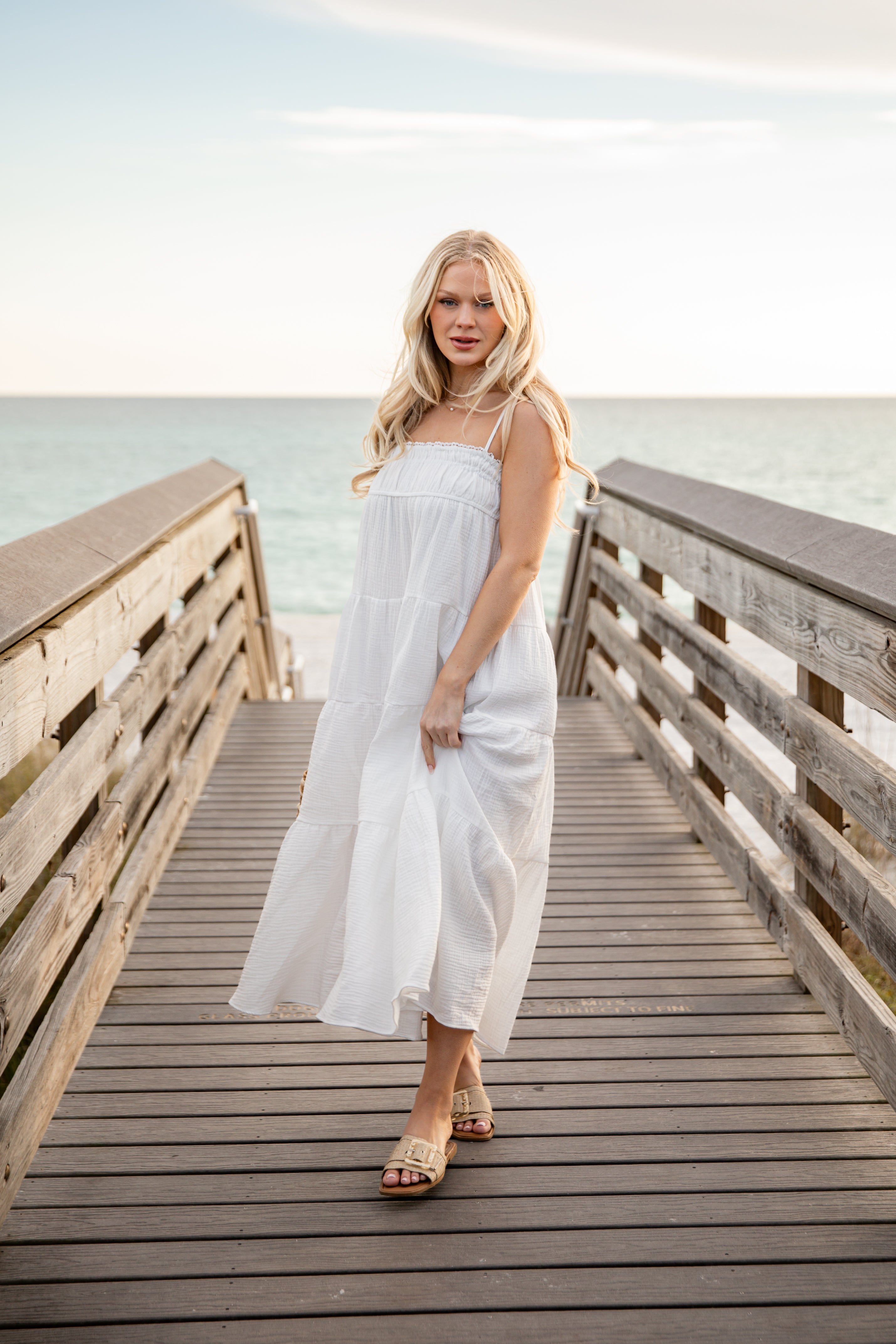 Woman in a white dress standing on a wooden pier by the sea.