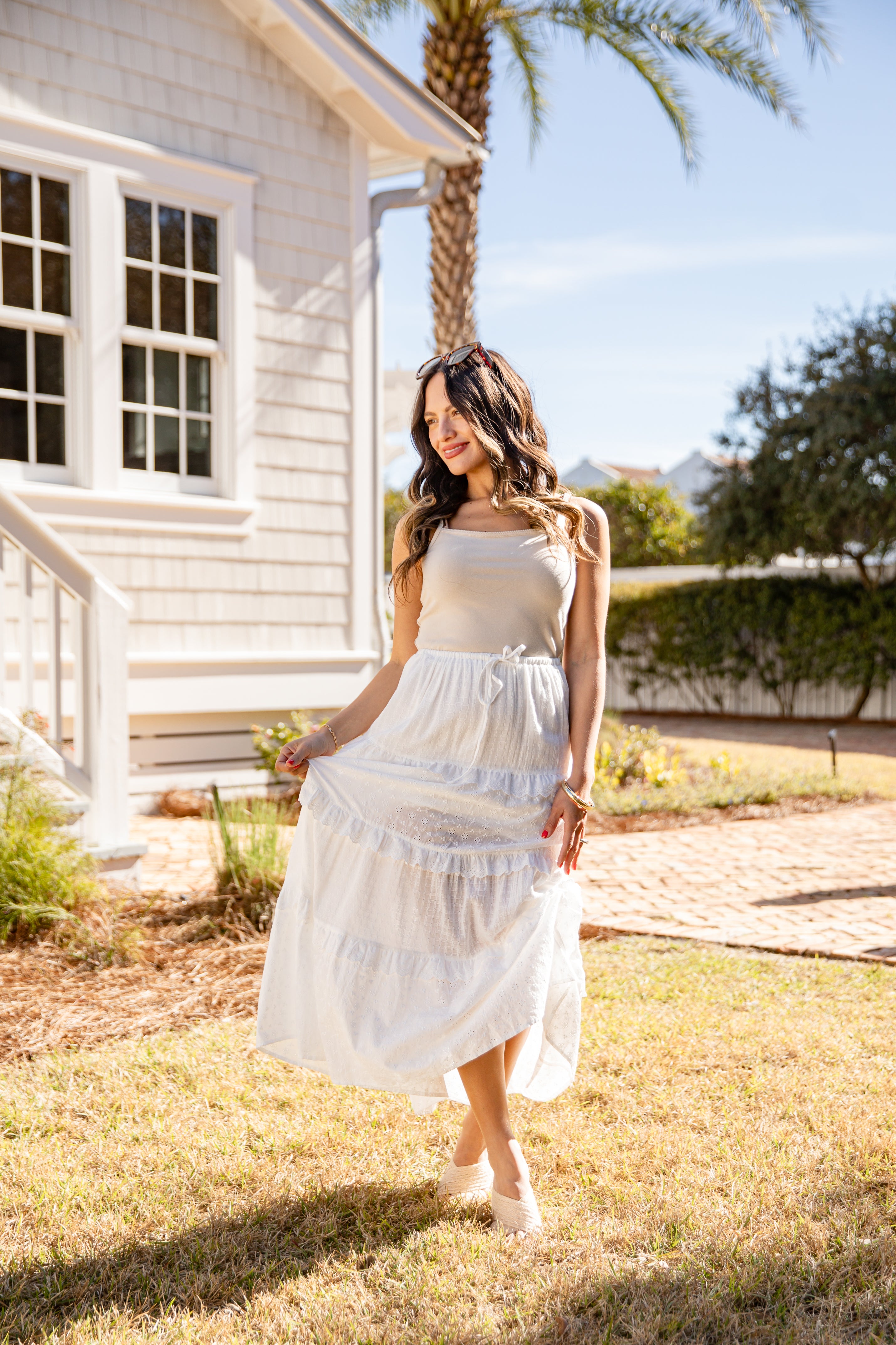 Woman in a white dress standing in a garden with a house and palm tree in the background